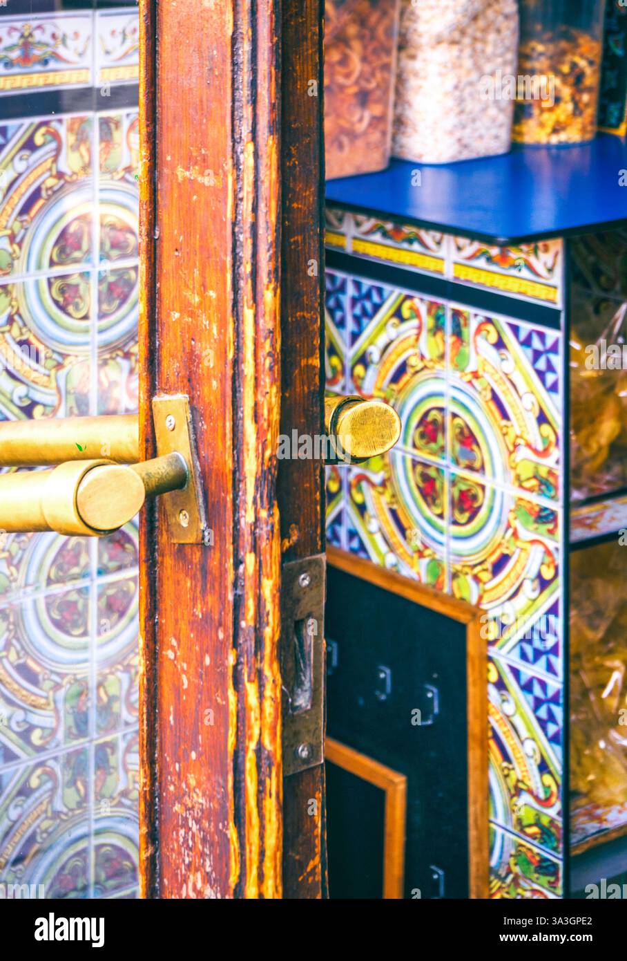 Una porta di legno intemprata con maniglie in ottone si apre per rivelare piastrelle di ceramica colorata che decorano l'interno di una tradizionale taverna spagnola. Foto Stock