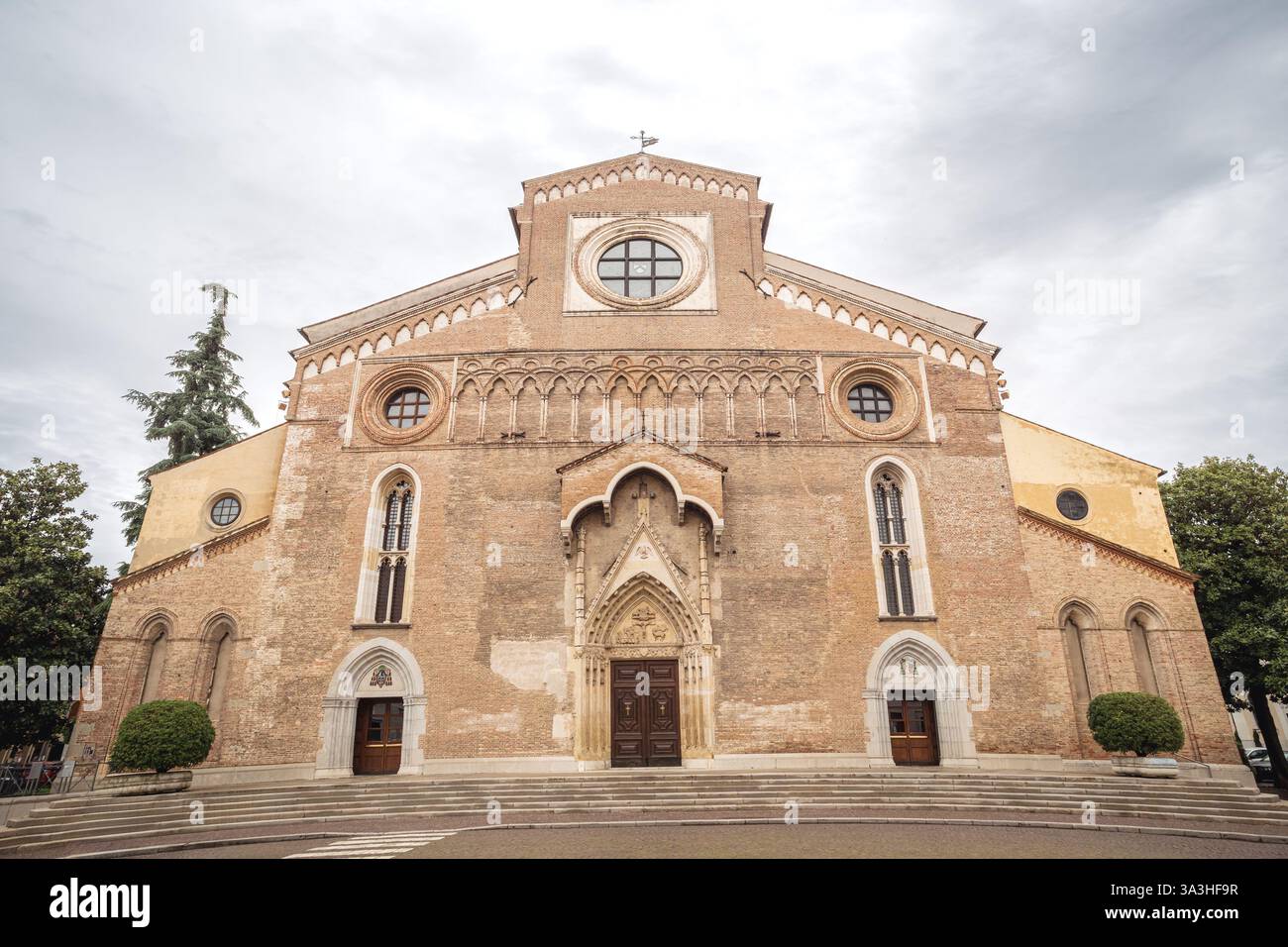 Una vista frontale della Cattedrale di Udine, in Italia, che presenta la sua storica facciata in mattoni, finestre ad arco e intricati dettagli gotici sotto un cielo nuvoloso Foto Stock