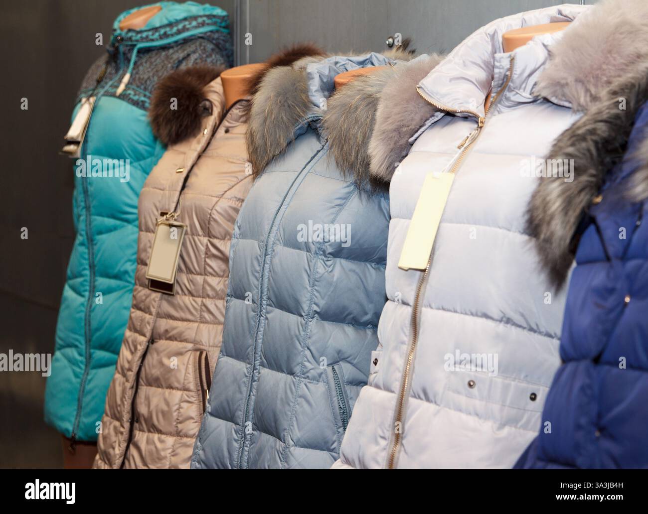Fila di giacche invernali con colletti in pelliccia su manichini, in vari colori, su uno sfondo interno. Concetto di outerwear alla moda Foto Stock