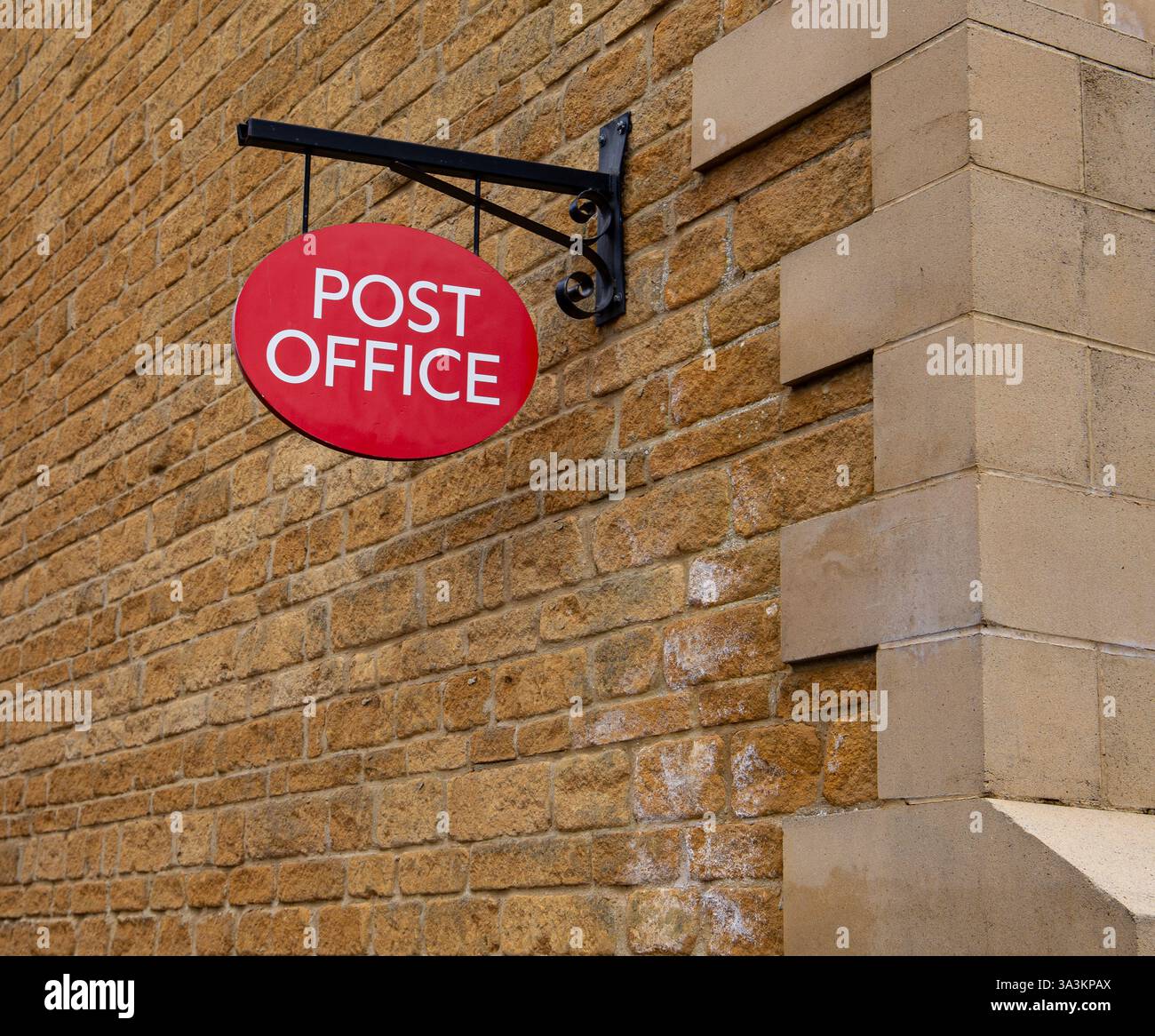 Cartello rosso dell'ufficio postale attaccato a un muro di pietra di un edificio con supporto in ferro d'epoca Foto Stock