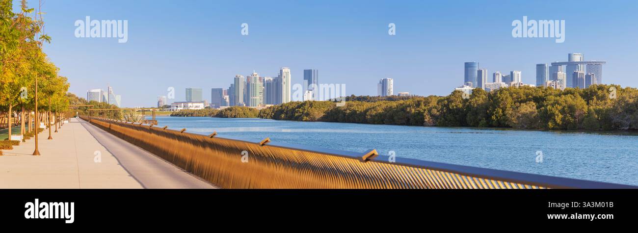 Vista panoramica del passaggio pedonale del parco di mangrovie con il moderno skyline di Abu Dhabi, caratterizzato da vegetazione lussureggiante e da un tranquillo corso d'acqua Foto Stock