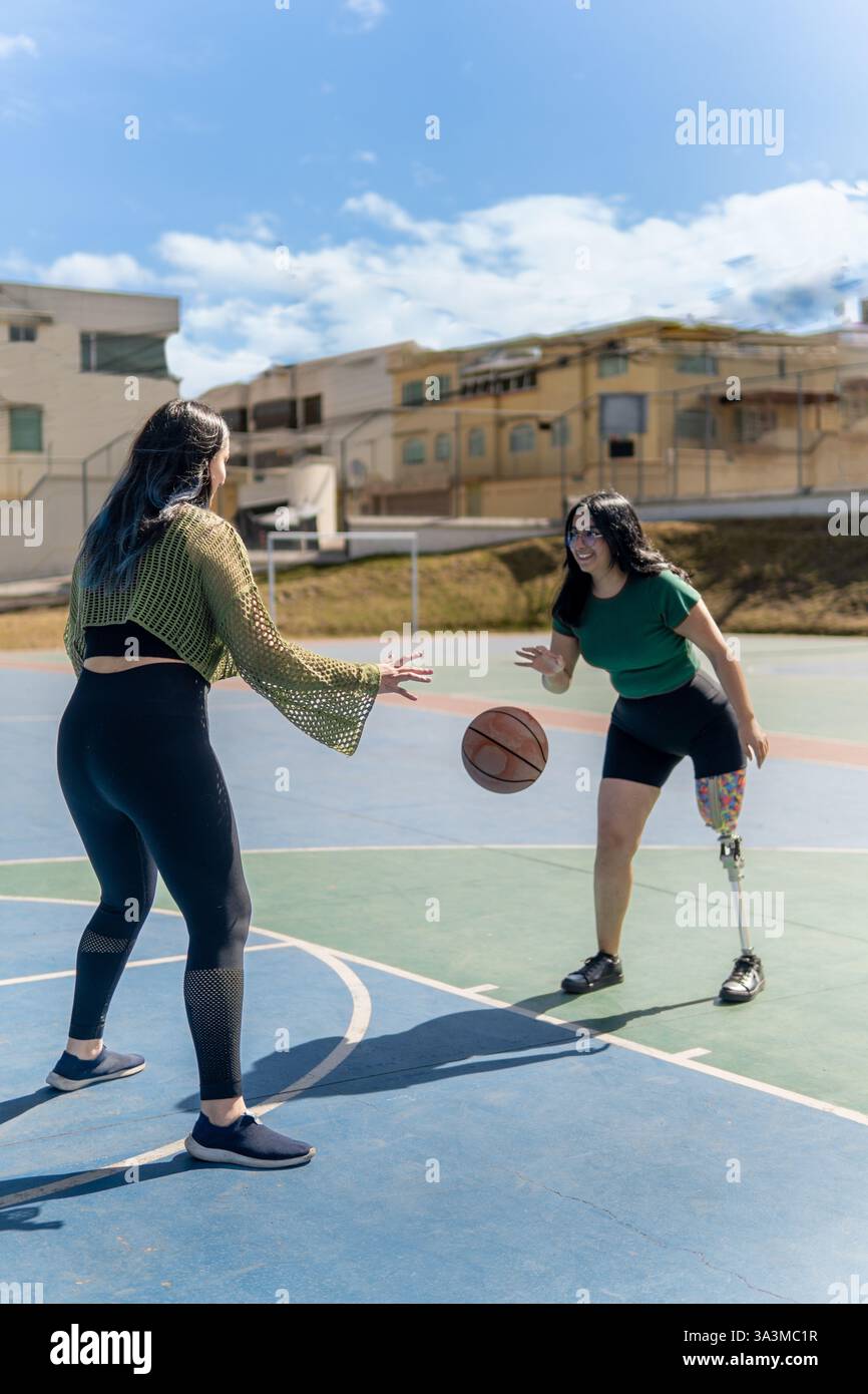 Due giovani donne si divertono a giocare a basket su un campo all'aperto, dimostrando inclusività e sportività Foto Stock