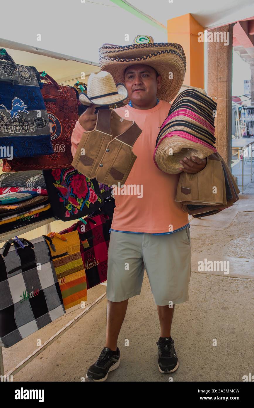 Un venditore maschile che tiene cesti e indossa tre cappelli da cowboy a teglia larga sulla testa vende i suoi prodotti a Nuevo Progreso, Tamaulipas, Messico. Foto Stock
