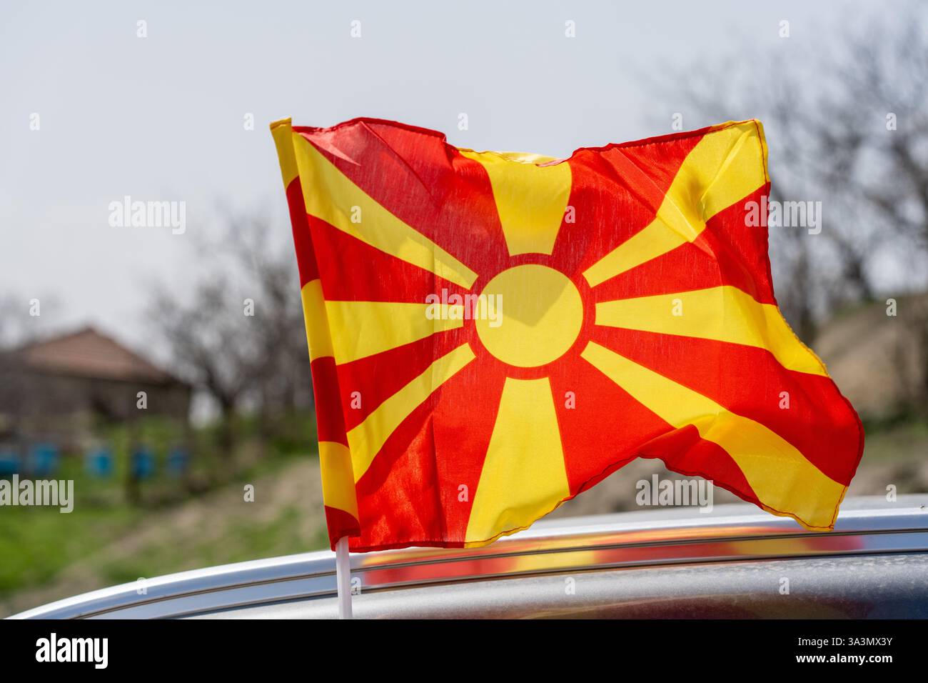 Bandiera macedone nel vento. Nel villaggio. Ambiente rurale. Cielo sfocato giorno. Foto Stock