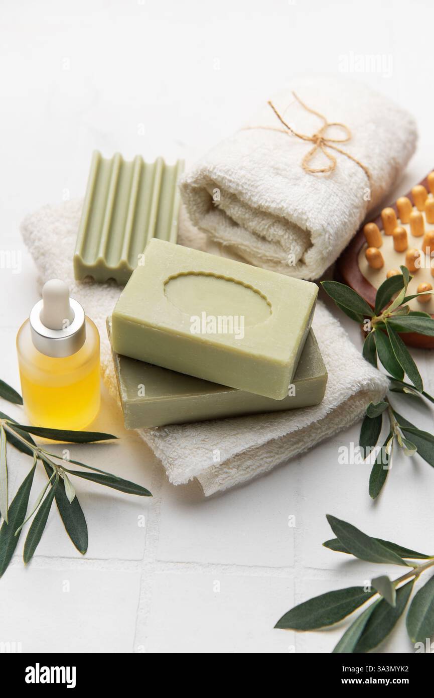 Sapone con olio d'oliva, spazzola per massaggi, olio essenziale e asciugamani bianchi creano un rilassante ambiente termale Foto Stock