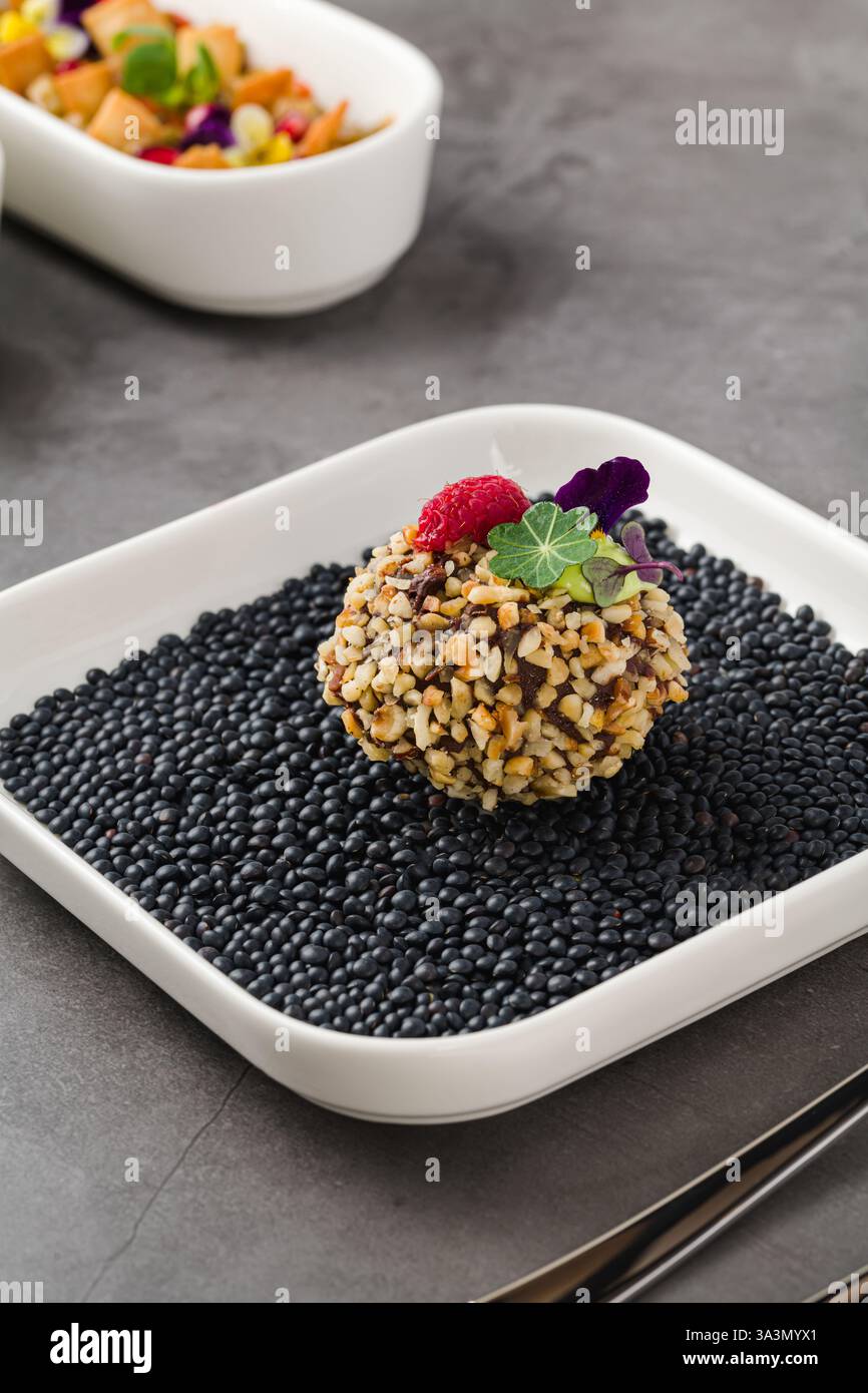 Tartufo foie gras gourmet ricoperto di noci tritate, guarnito con lamponi e fiori commestibili, servito su lenticchie nere Foto Stock