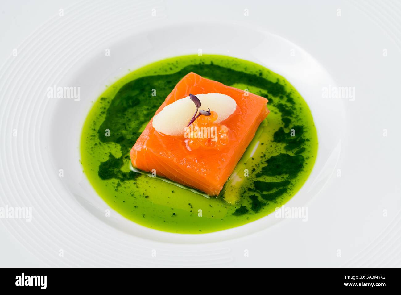 Filetto di salmone sous-vide con capriolo di pesce, guarnito con sorbetto e microgreen, servito su una vivace salsa alle erbe verdi Foto Stock