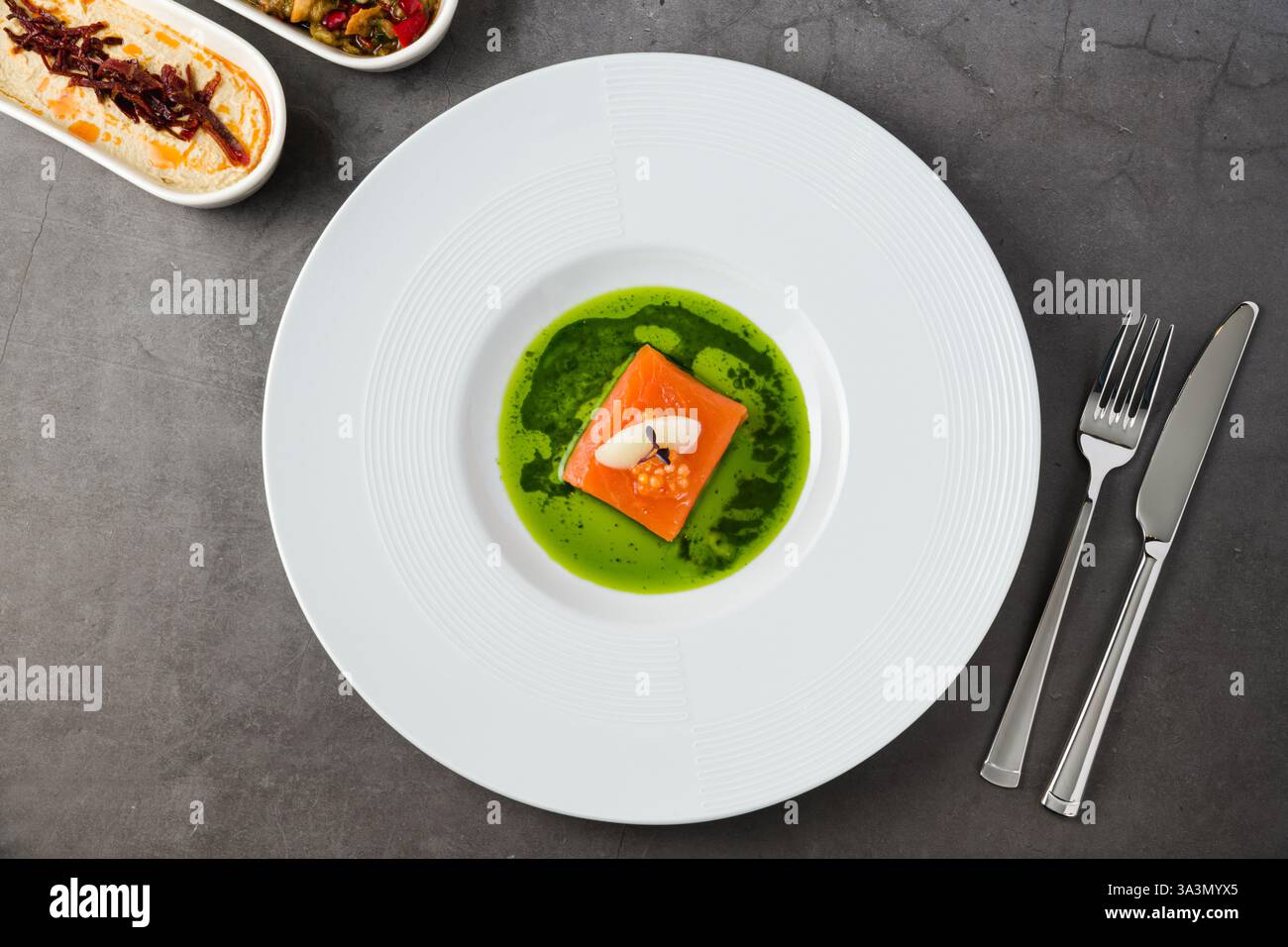 Filetto di salmone sous-vide con capriolo di pesce, guarnito con sorbetto e microgreen, servito su una vivace salsa alle erbe verdi Foto Stock