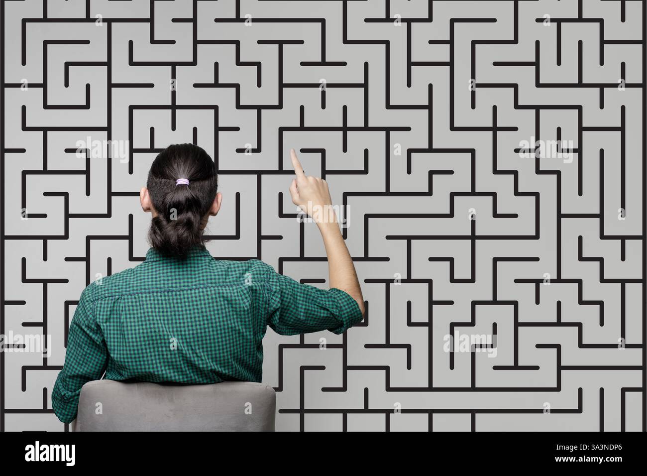 Una donna è in piedi vicino a un muro con un disegno di un labirinto e puntando su di esso. Concetto di brainstorming, pensiero, risoluzione dei problemi Foto Stock