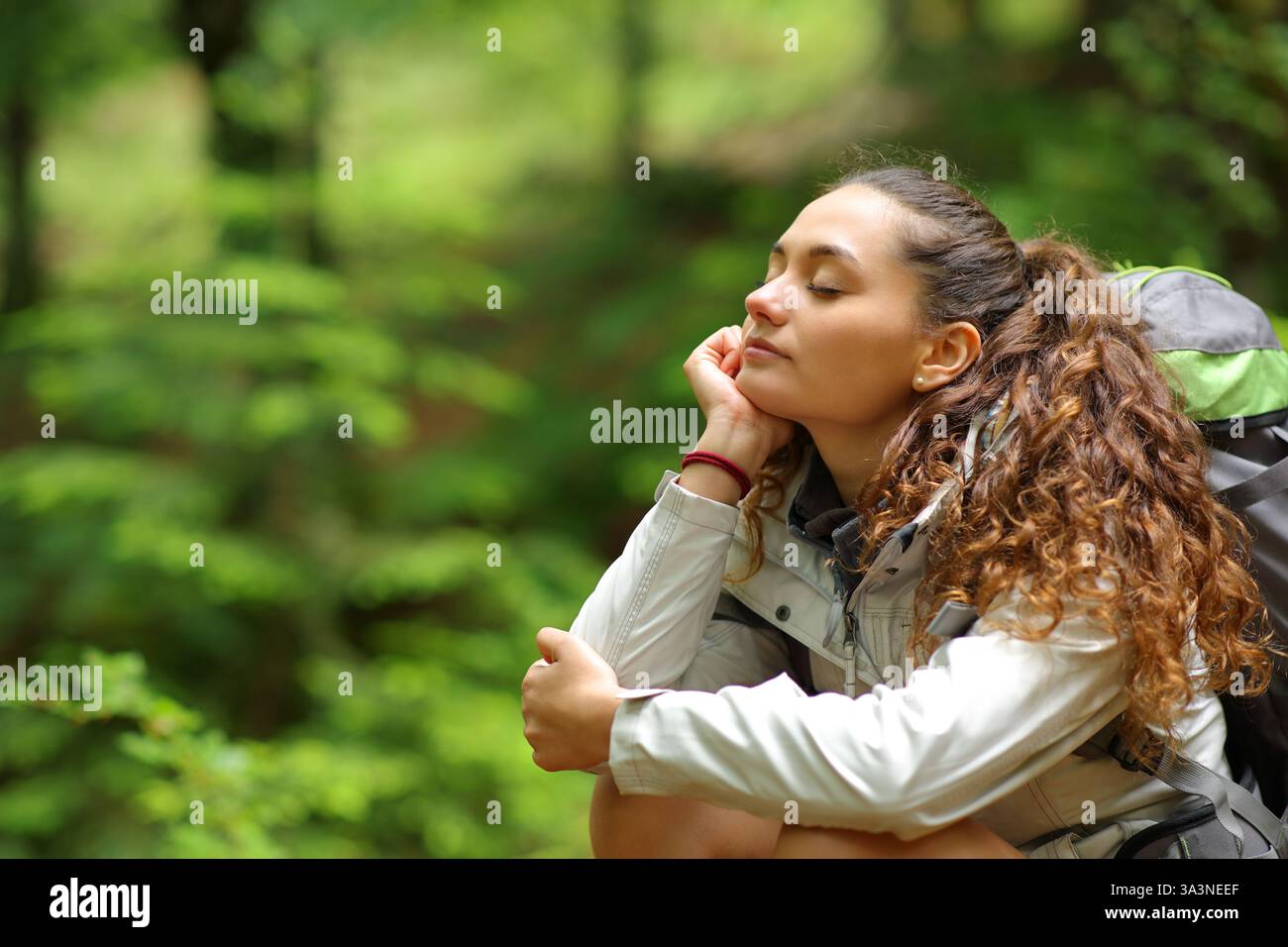 Escursionista riposante e rilassante a occhi chiusi seduto in una foresta da solo Foto Stock