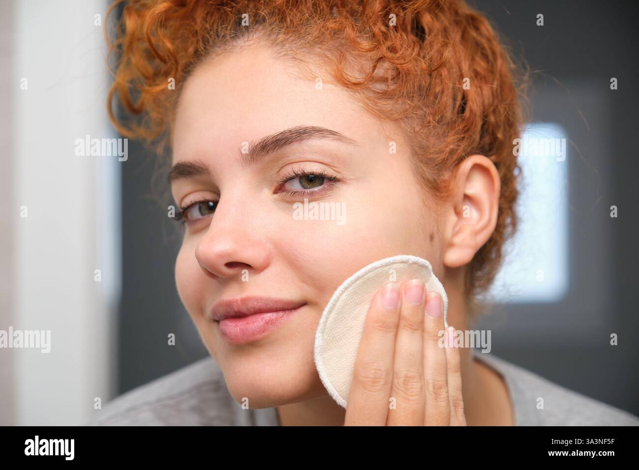 Giovane donna che pulisce il viso con un panno riutilizzabile per rimuovere il trucco Foto Stock