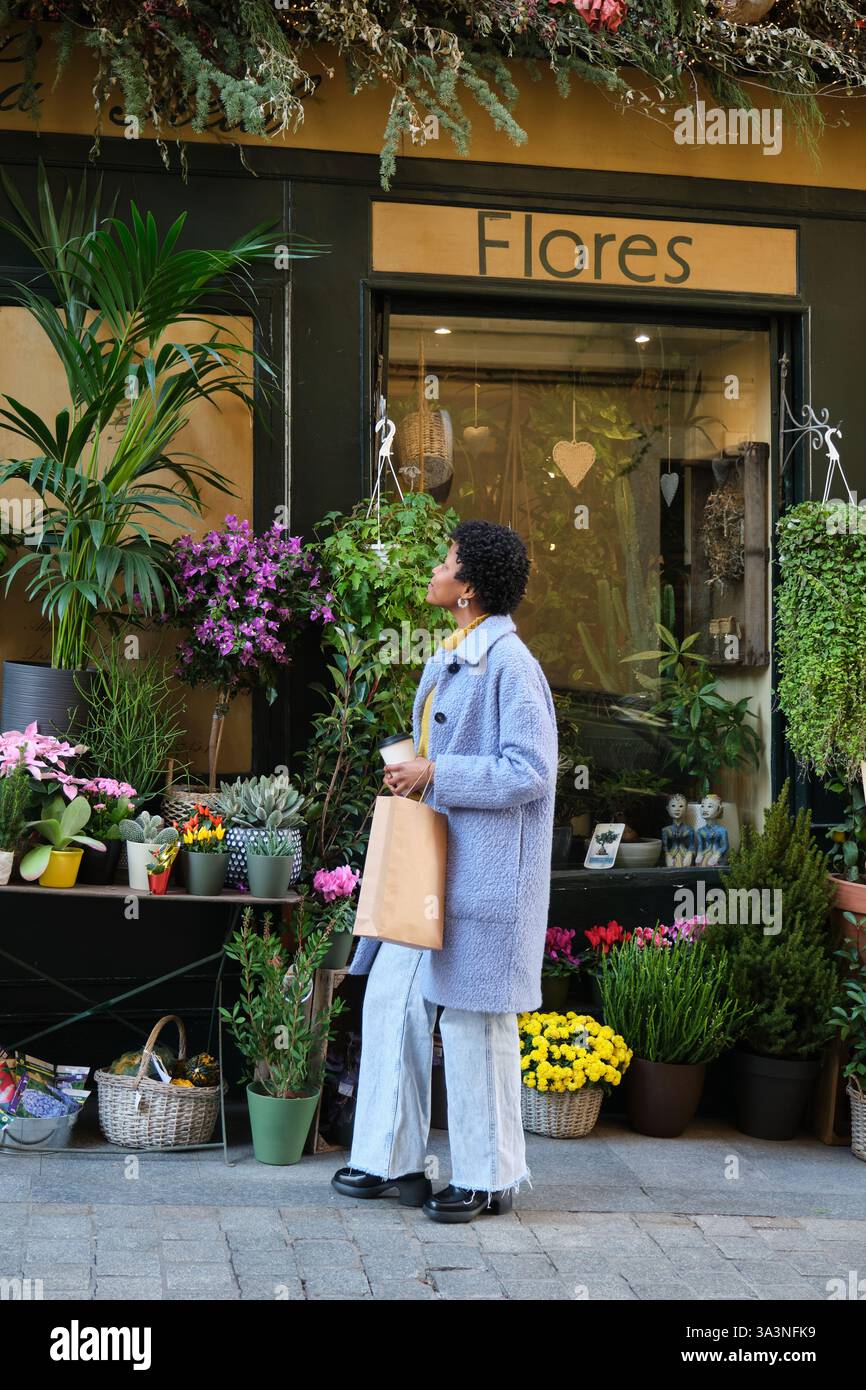 Donna che ammira i fiori di fronte a un negozio di fiori Foto Stock