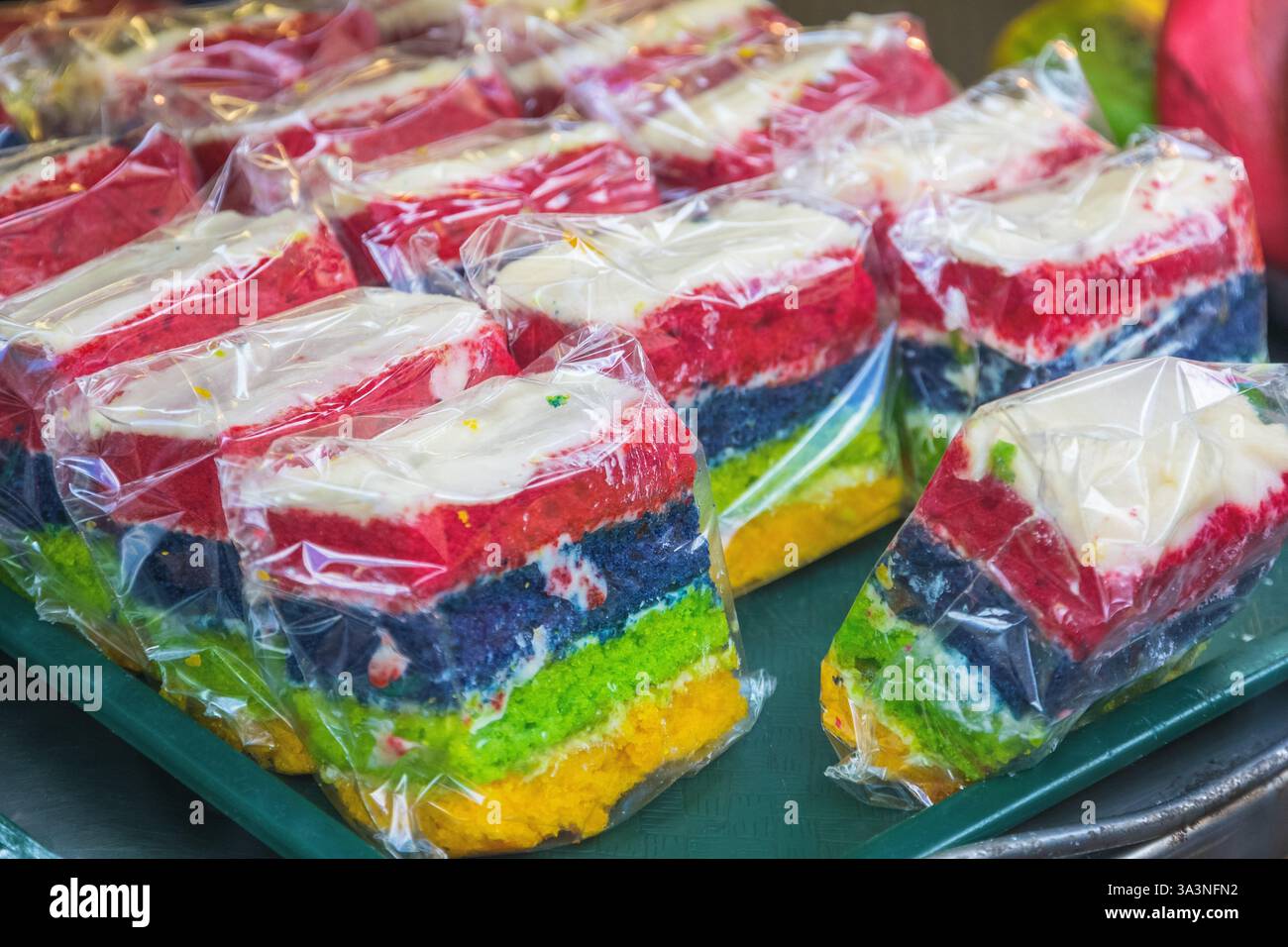 Fette di torte di spugna arcobaleno esposte al Brick Lane Market di Londra Foto Stock