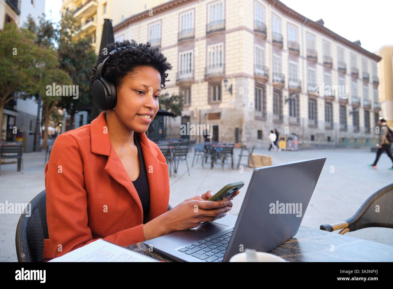Donna che utilizza un computer portatile e uno smartphone in un bar all'aperto Foto Stock
