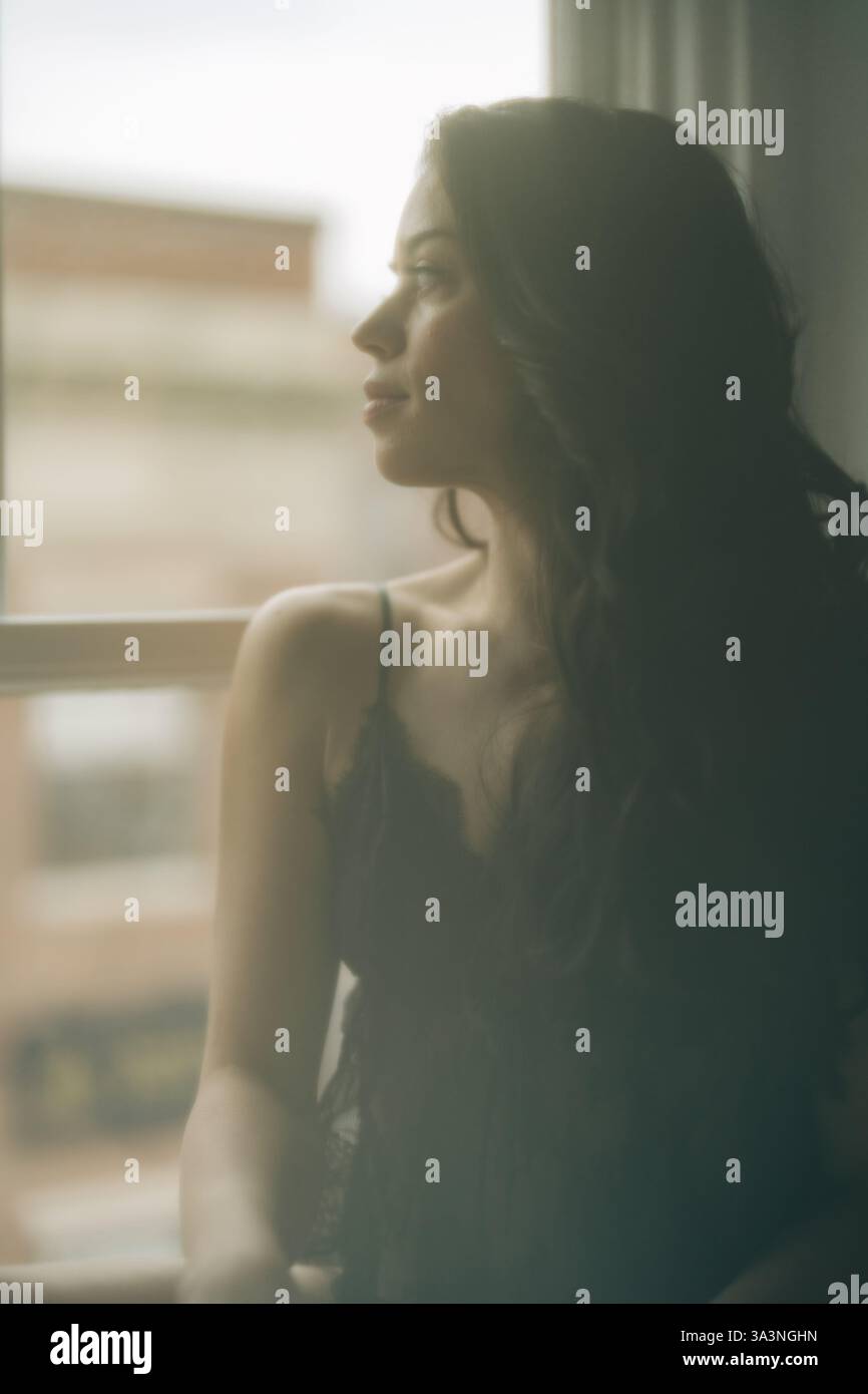 Donna in pizzo nero che guarda fuori dalla finestra, messa a fuoco morbida e illuminazione soffusa Foto Stock