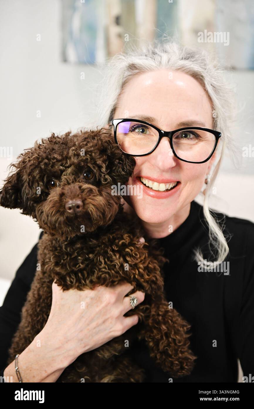Donna sorridente con occhiali che reggono una piccola pu marrone dai capelli ricci Foto Stock