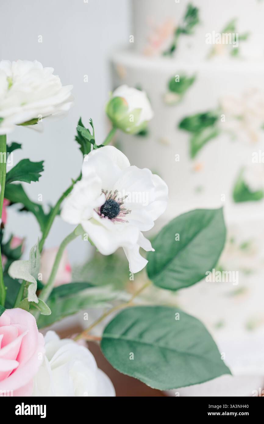 Composizione floreale bianca e rosa accanto a una torta sfocata a strati. Foto Stock
