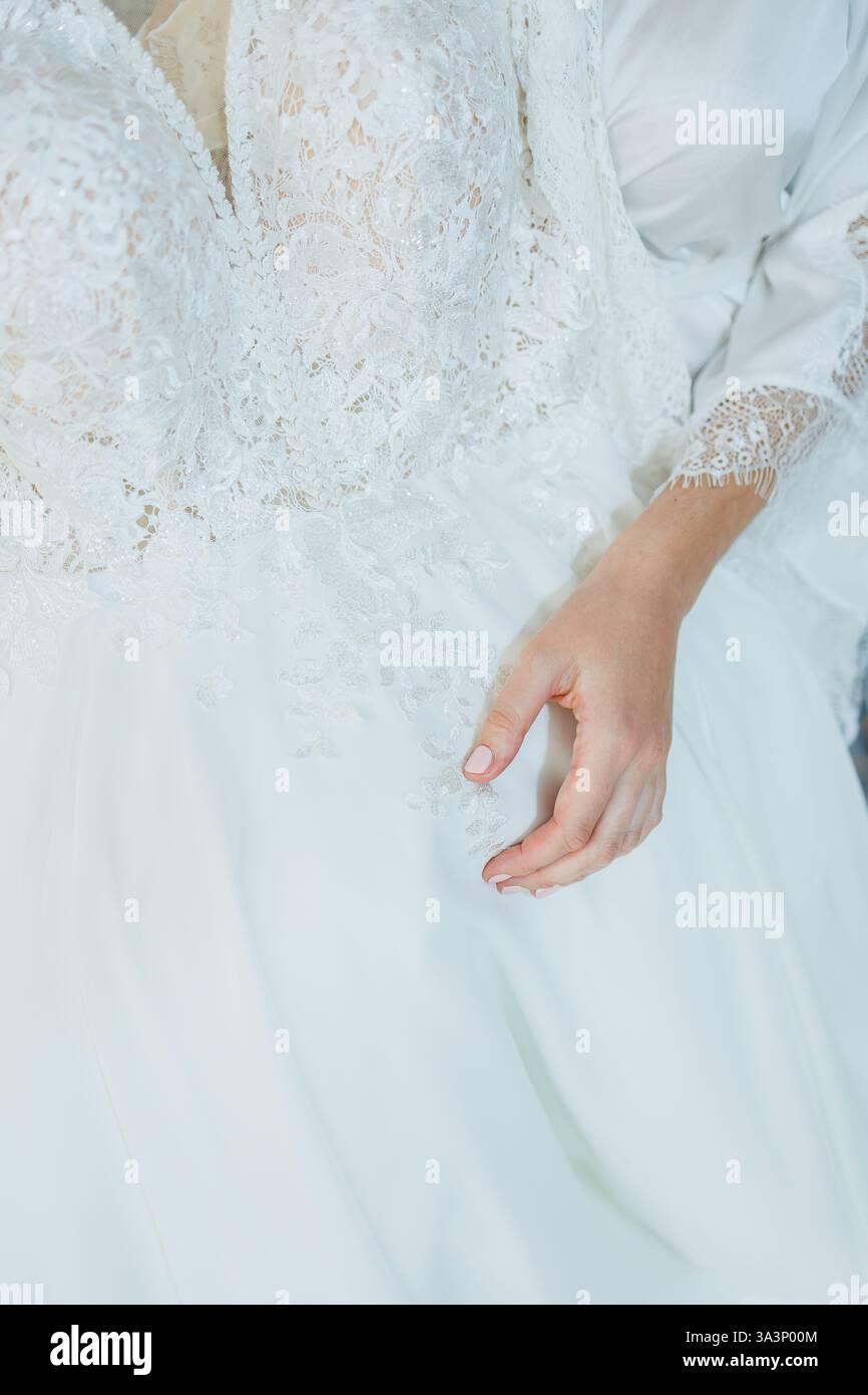 Una fotografia dettagliata di primo piano di un'elegante mano femminile che riposa con grazia su un bellissimo abito bianco che cattura l'attenzione Foto Stock