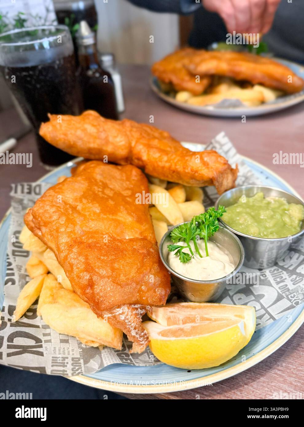 Un piatto di pesce e patatine fritte, servito con piselli moschi, salsa alla tartare e un spicchio di limone (erano deliziosi) Foto Stock