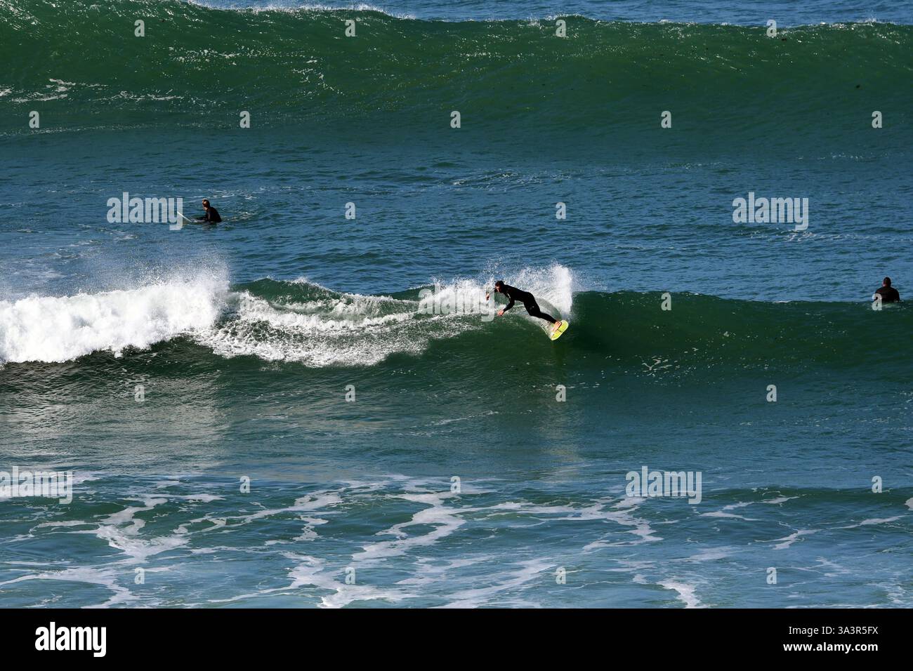 Surfista intagliando la sua tavola sull'acqua lasciando uno spruzzo dietro. Giornata di sole con acqua pulita, surf su un'onda verde in un ambiente tranquillo. Foto Stock