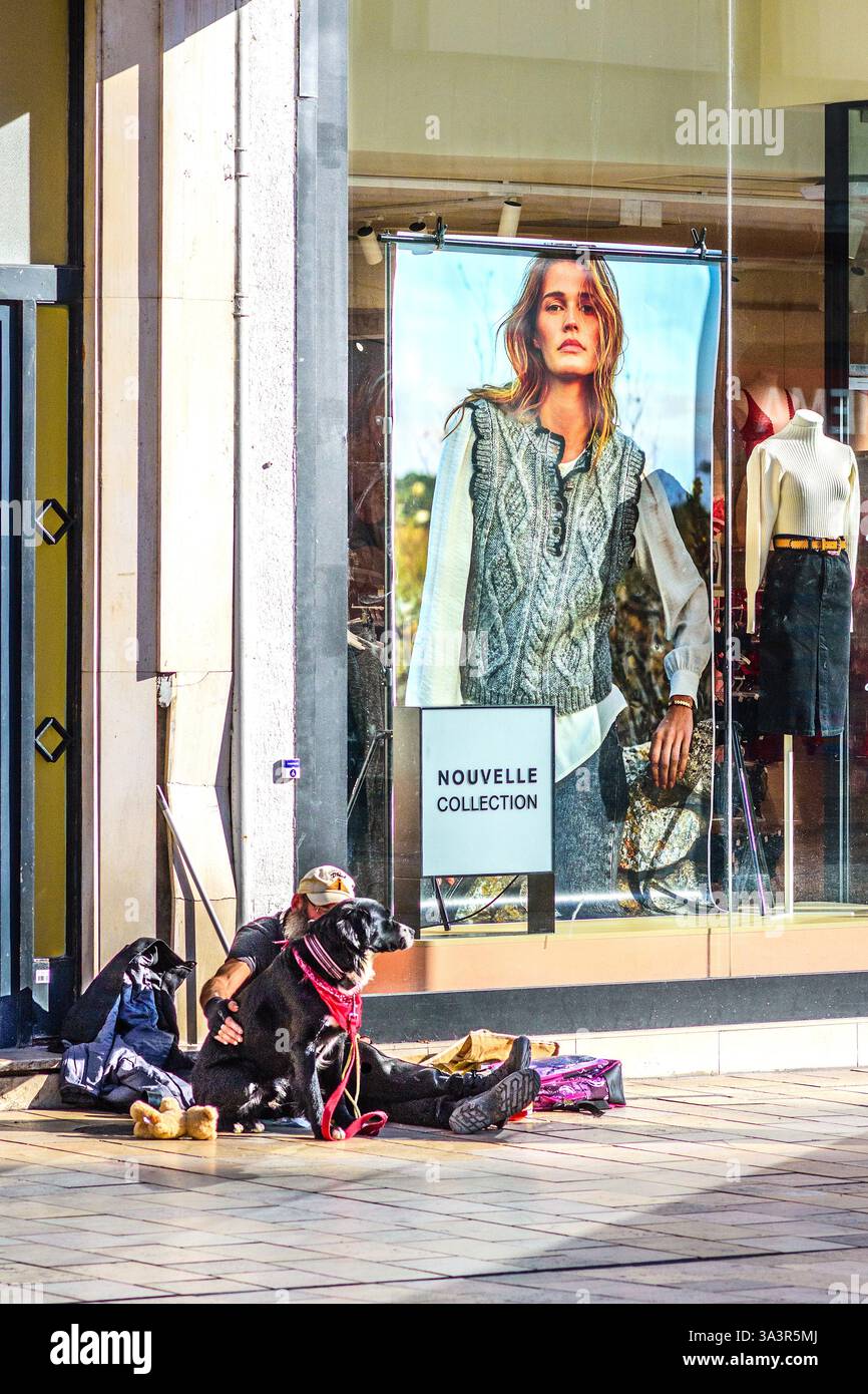 Senzatetto e cane seduti sul marciapiede all'esterno della boutique di moda con poster della modella - Tours, Indre-et-Loire (37), Francia. Foto Stock