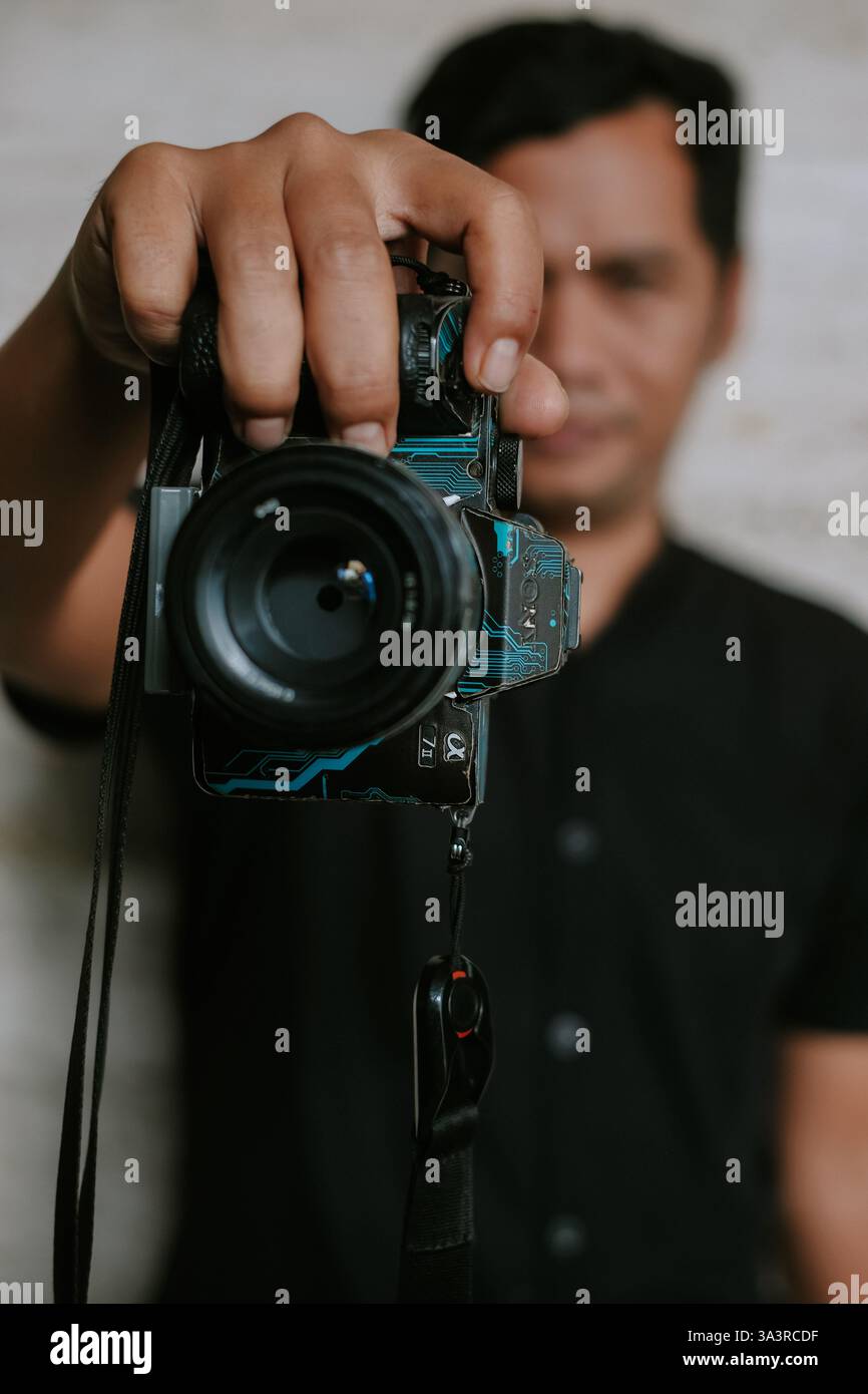Ritratto di un uomo che tiene in mano una fotocamera digitale, concentrandosi sulla cattura del momento. La telecamera ha un design personalizzato del circuito, una miscela di elettroni Foto Stock