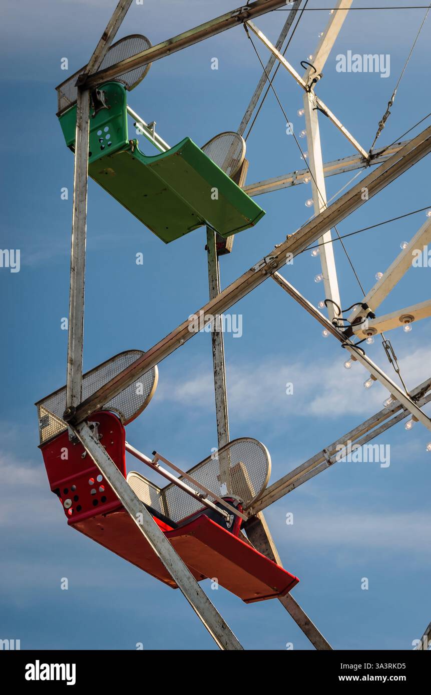 Vista dal basso verso il cielo di due antichi sedili rossi e verdi della ruota panoramica e della struttura in metallo su un cielo blu. Foto Stock