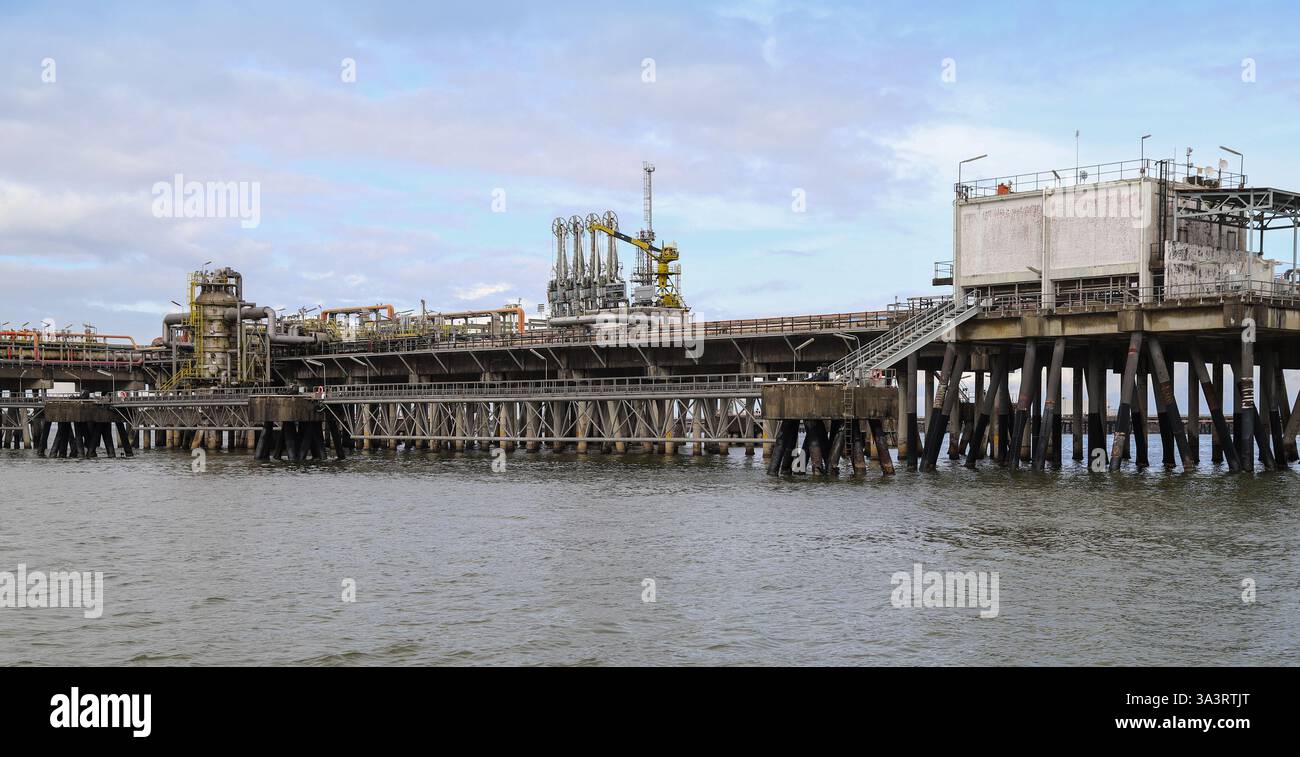Impianto industriale situato su un molo sopra un corpo idrico, caratterizzato da macchinari e strutture legati ai processi industriali messi in mostra contro un cle Foto Stock