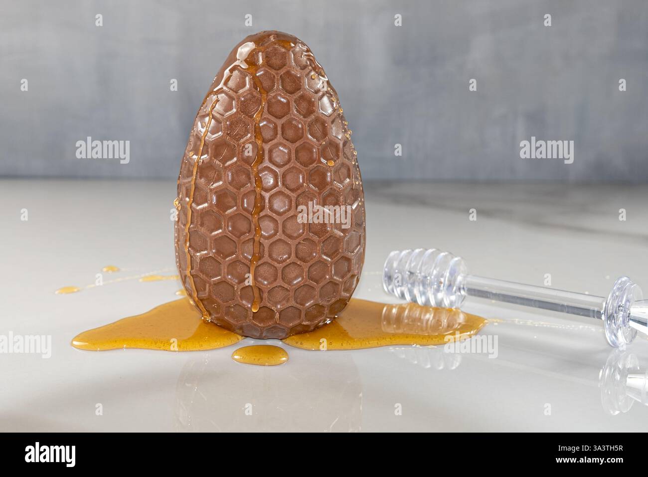 Primo piano dell'uovo di pasqua al cioccolato con miele su marmo. Foto Stock