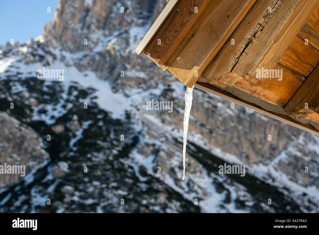 Una pittoresca scena di una montagna innevata con un tetto in legno e ghiaccioli appesi ad essa. La scena è tranquilla e rilassante, mentre i ghiaccioli lentamente dr Foto Stock