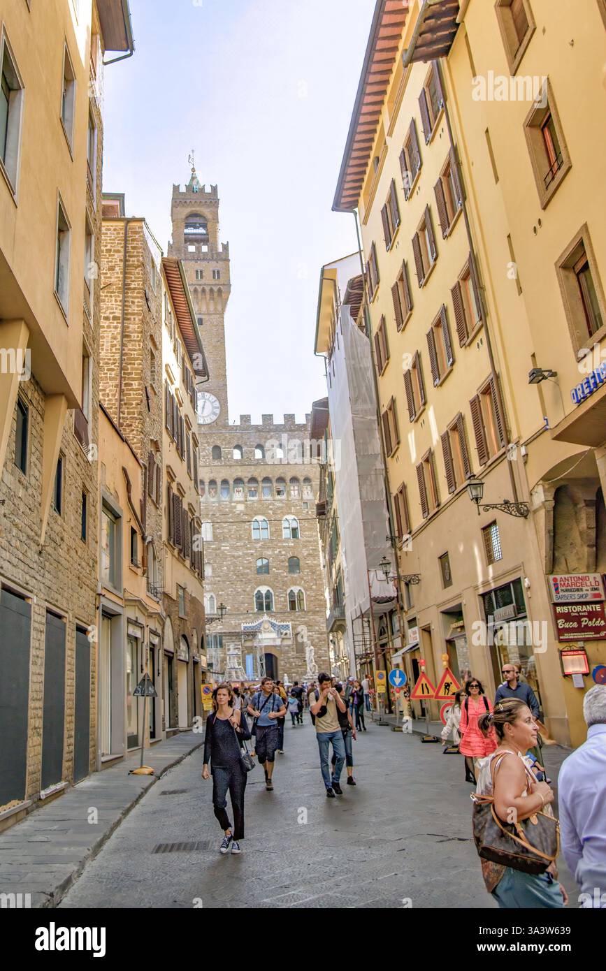 Italia 2022 turisti che camminano lungo via dei Leoni verso Palazzo Vecchio e la sua iconica Torre Arnolfo a Firenze, Italia. Lo storico palazzo medievale Foto Stock