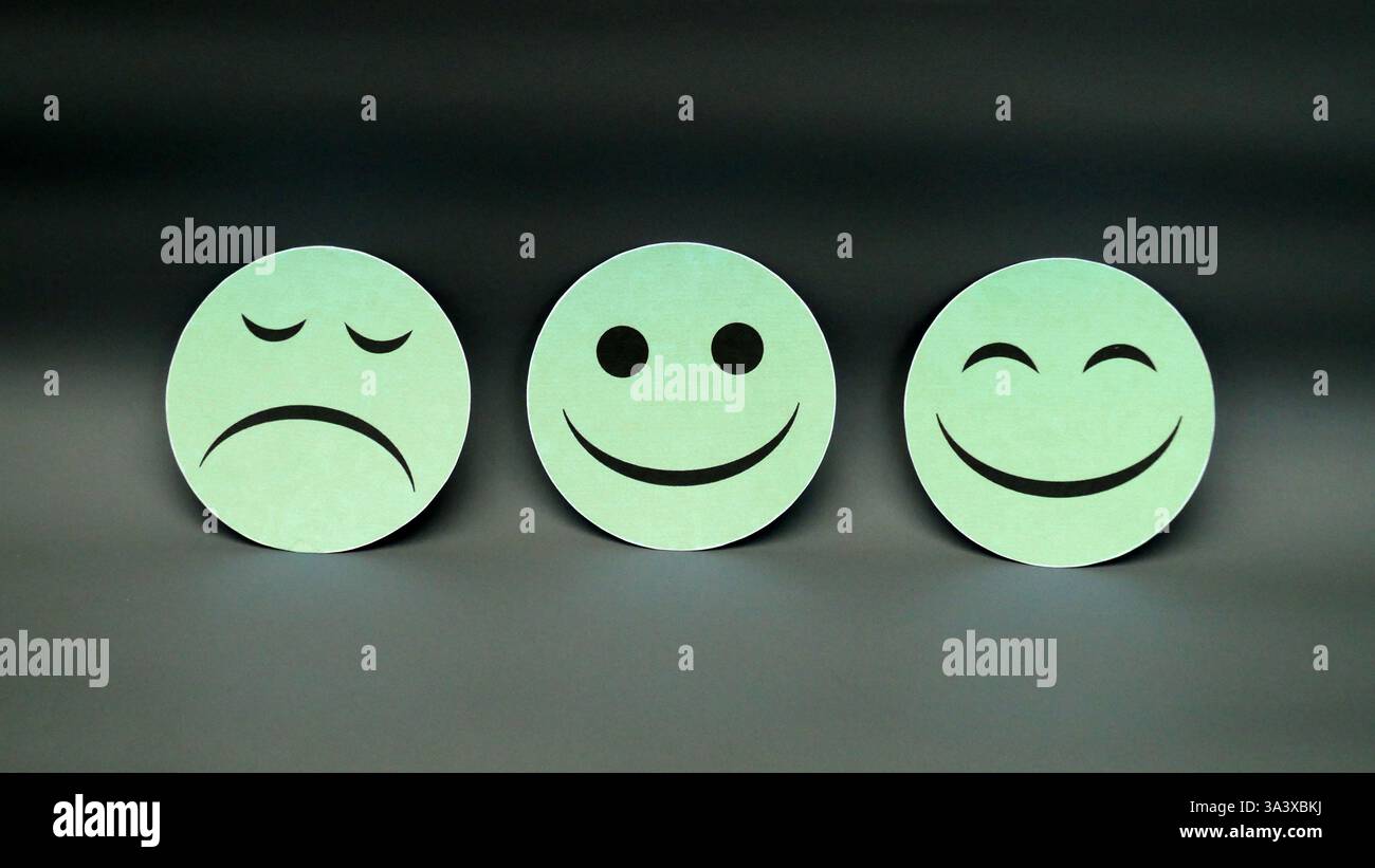 Tre facce di emozione bianca che mostrano espressioni SAD, Neutral e Happy su sfondo scuro che rappresentano i cambiamenti di umore Foto Stock
