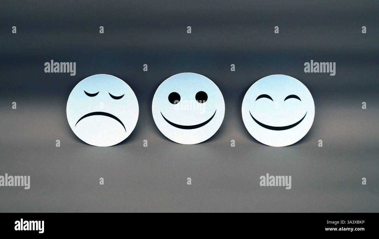 Tre facce di emozione bianca che mostrano espressioni SAD, Neutral e Happy su sfondo scuro che rappresentano i cambiamenti di umore Foto Stock