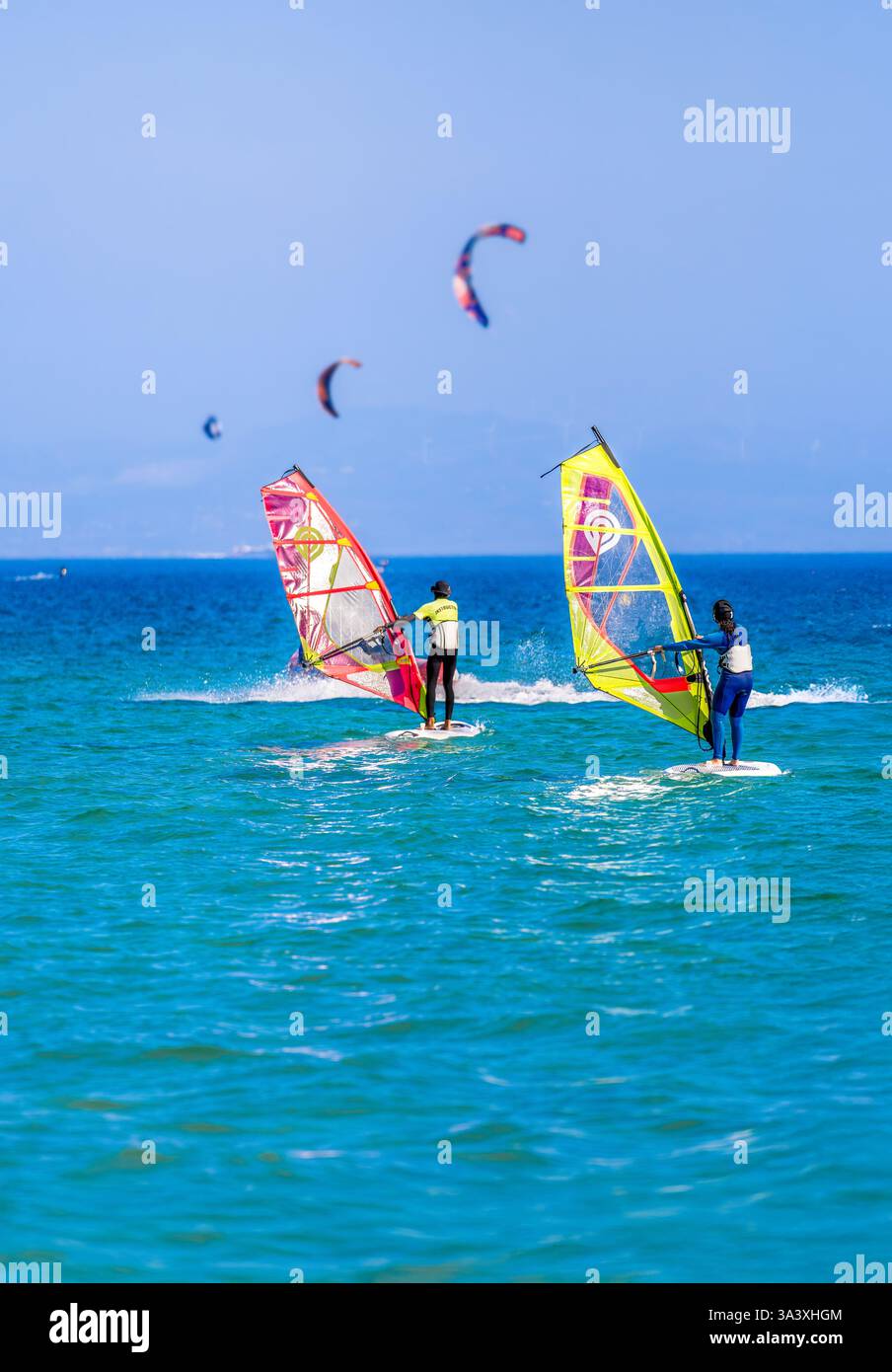 Istruttore di windsurf surf surf e insegnamento a una donna principiante nelle acque turchesi dell'oceano a Tarifa, in Spagna, sulla spiaggia di Bolonia, con aquiloni da kitesurfer Foto Stock