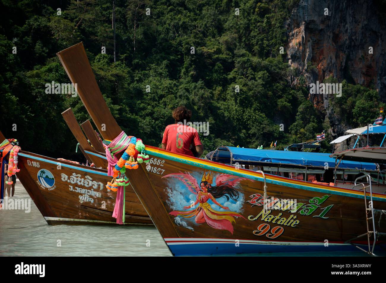 Un giovane operaio si siede di fronte a una barca a coda lunga decorata in modo vibrante Foto Stock