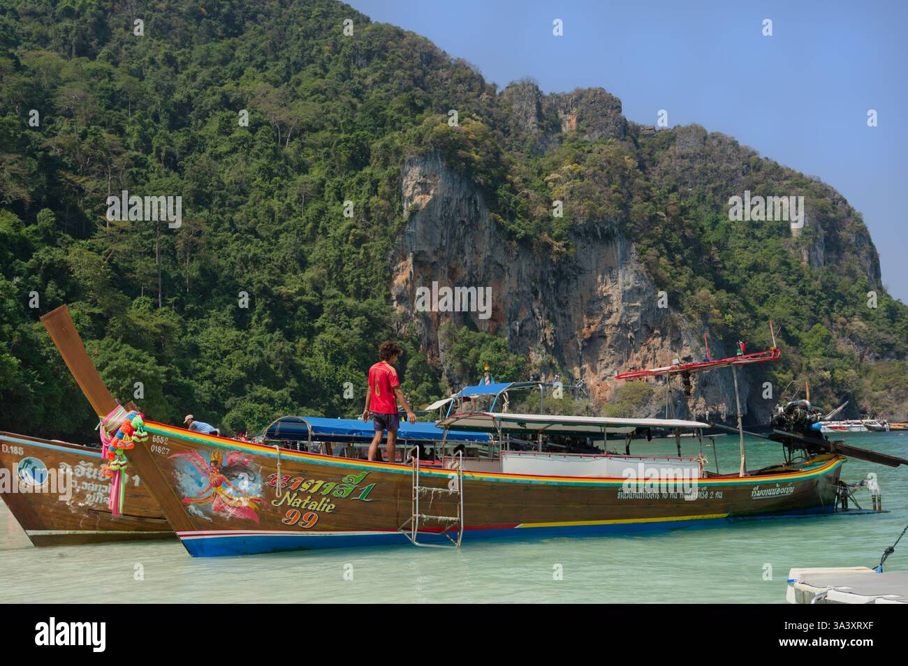 Un giovane pescatore attende su una barca a coda lunga decorata sulla riva del parco delle scimmie di Dabizha Foto Stock
