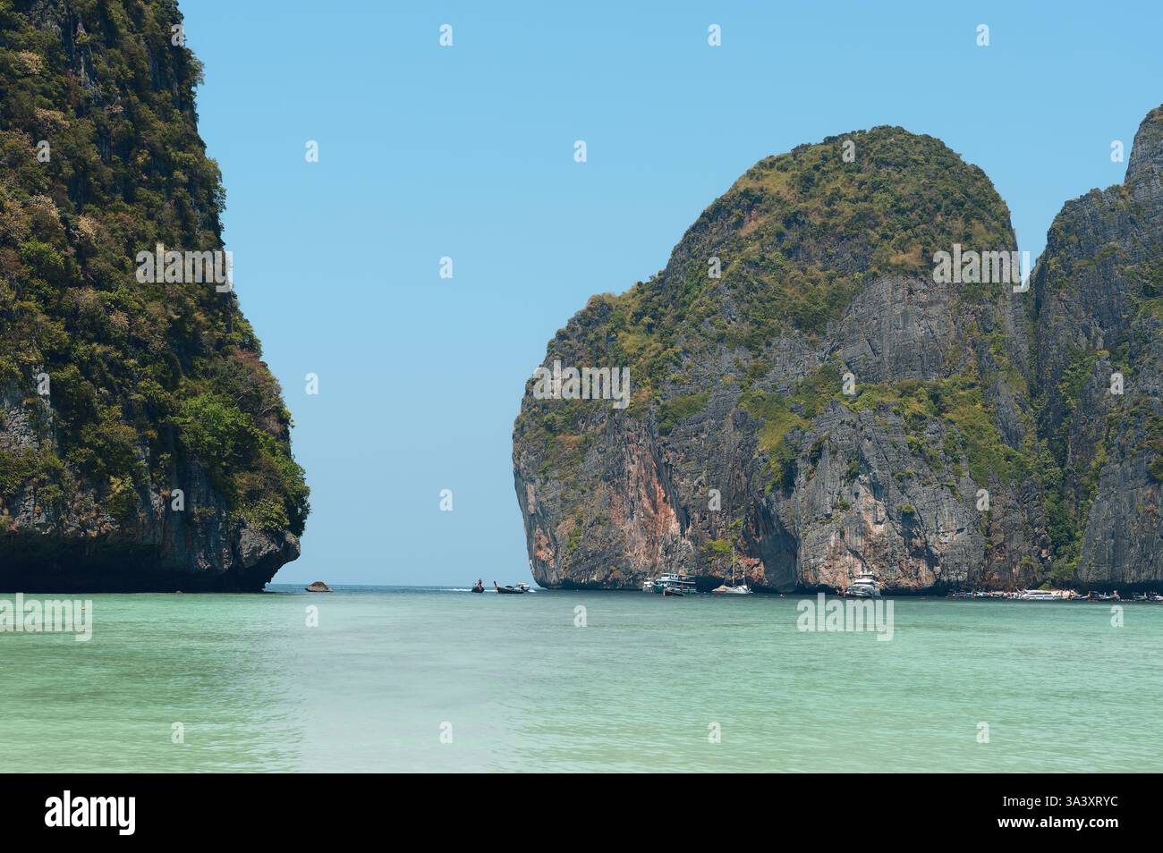 Le torreggianti scogliere calcaree incorniciano le acque turchesi di Maya Bay, con barche che galleggiano in lontananza Foto Stock