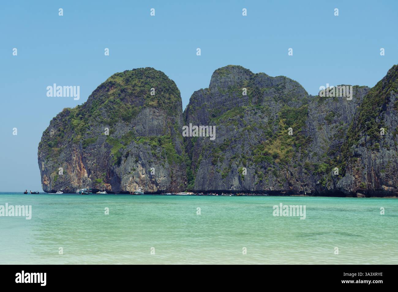 Le scogliere calcaree frastagliate sorgono dalle acque turchesi di Maya Bay, mentre le barche si radunano vicino alla riva di questo iconico paradiso tropicale Foto Stock