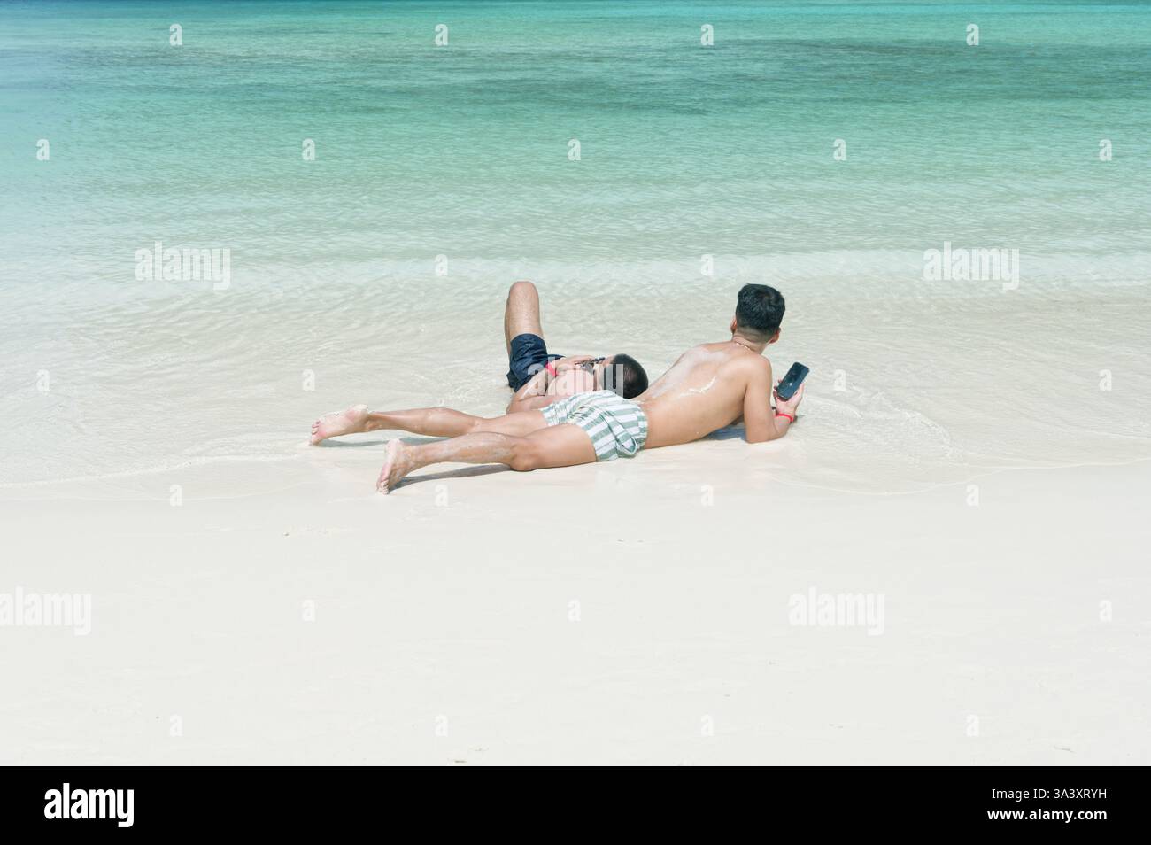 Una coppia gay si rilassa sulla spiaggia, adagiata sulla sabbia soffice di Maya Bay Foto Stock