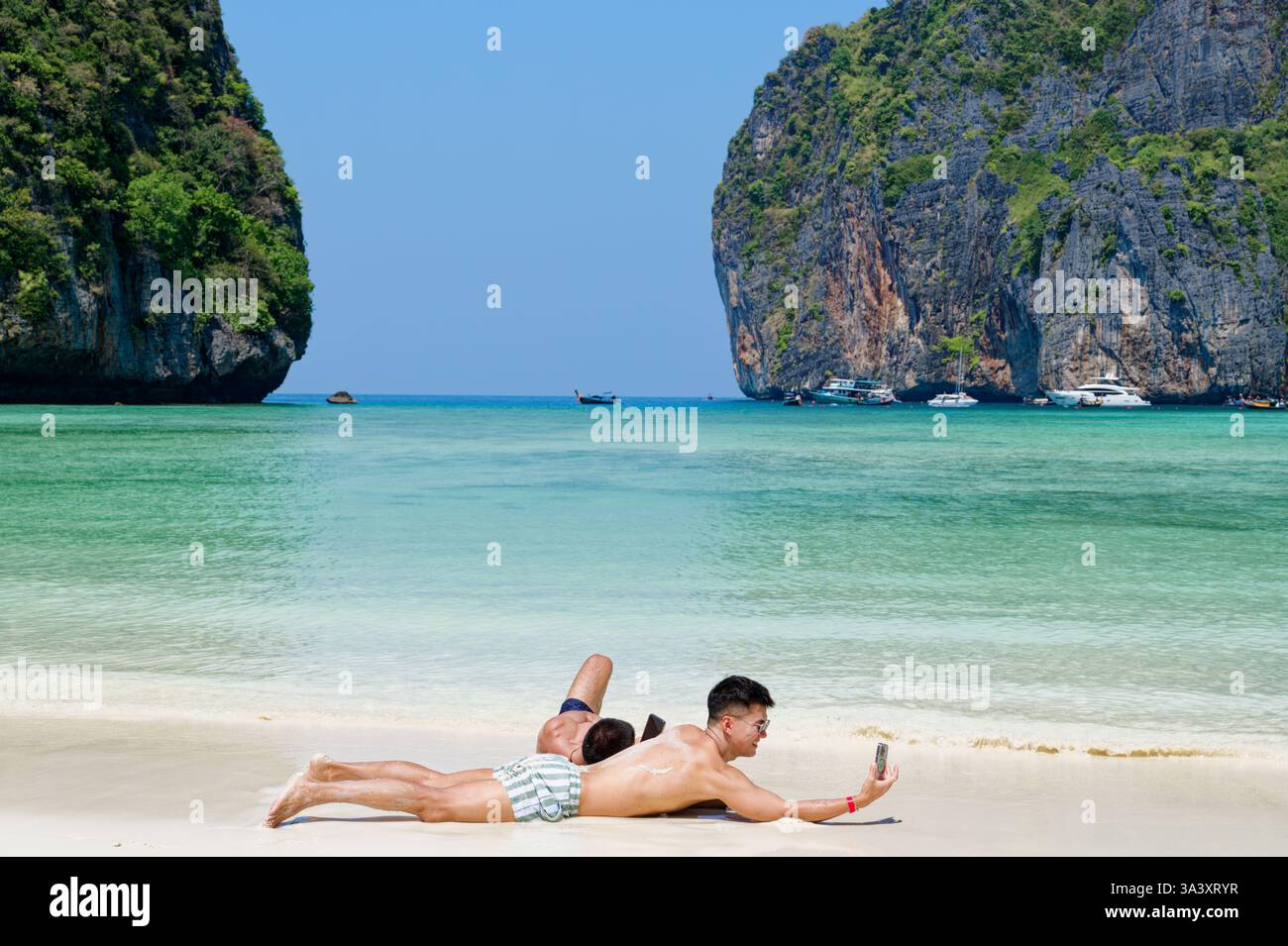 Due uomini si rilassano sulle sabbie morbide di Maya Bay mentre scattano un selfie Foto Stock