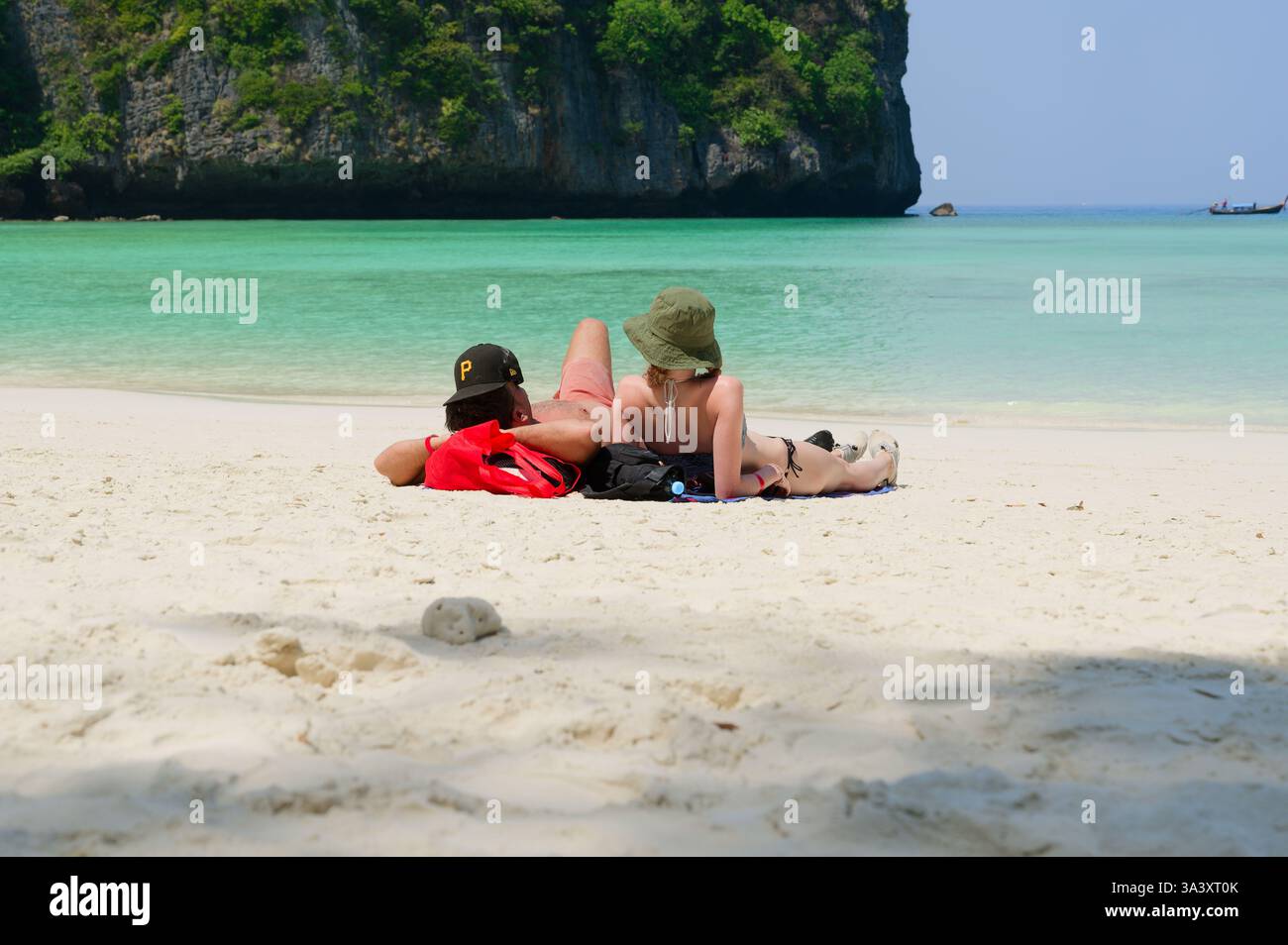 Una giovane coppia si rilassa sulle sabbie bianche di Maya Bay, osservando le acque turchesi Foto Stock