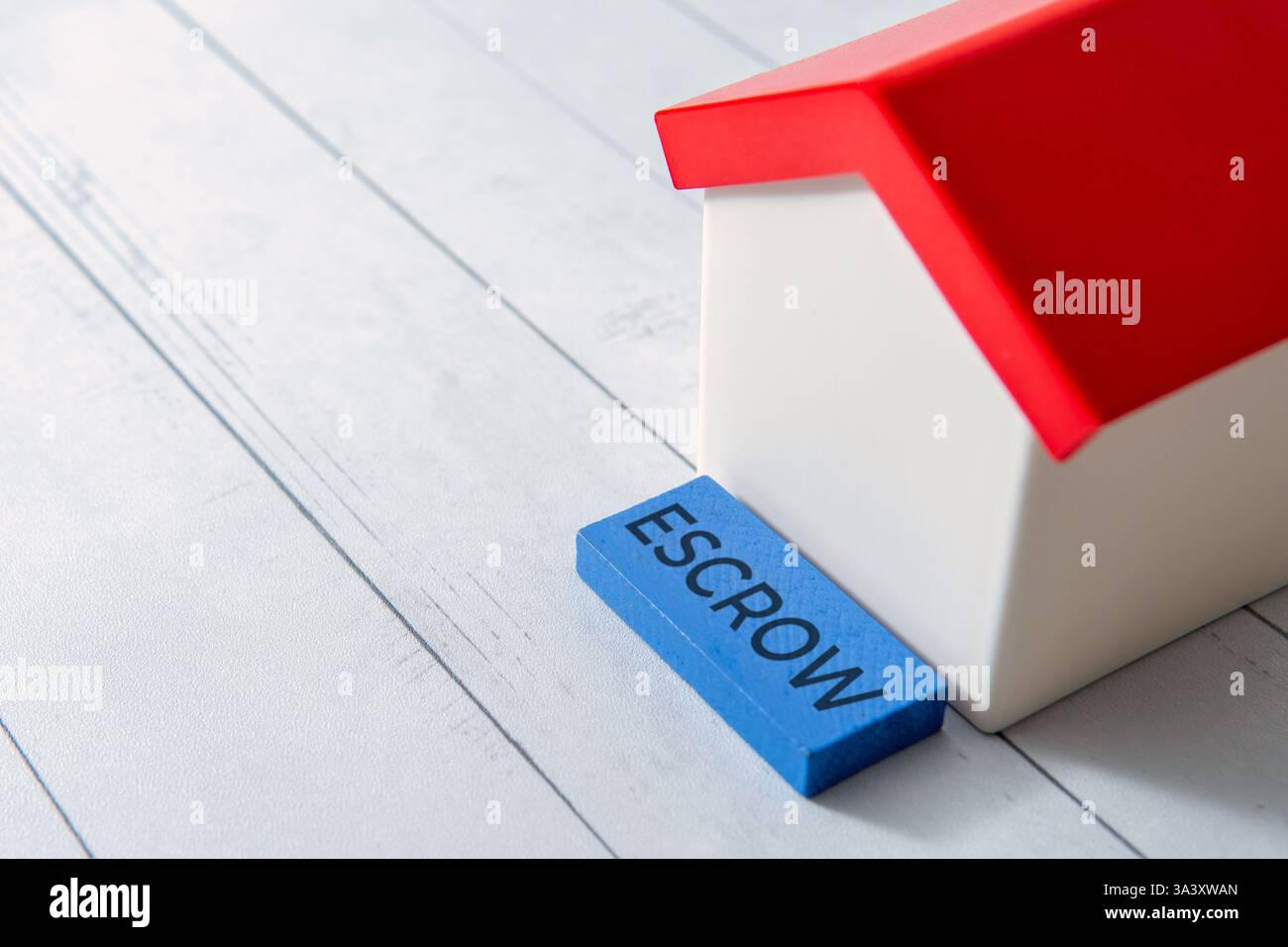 La parola "ESCROW" accanto a una piccola casa dei giocattoli. Operazioni immobiliari o concetto di sicurezza finanziaria. Copia spazio per il testo. Foto Stock