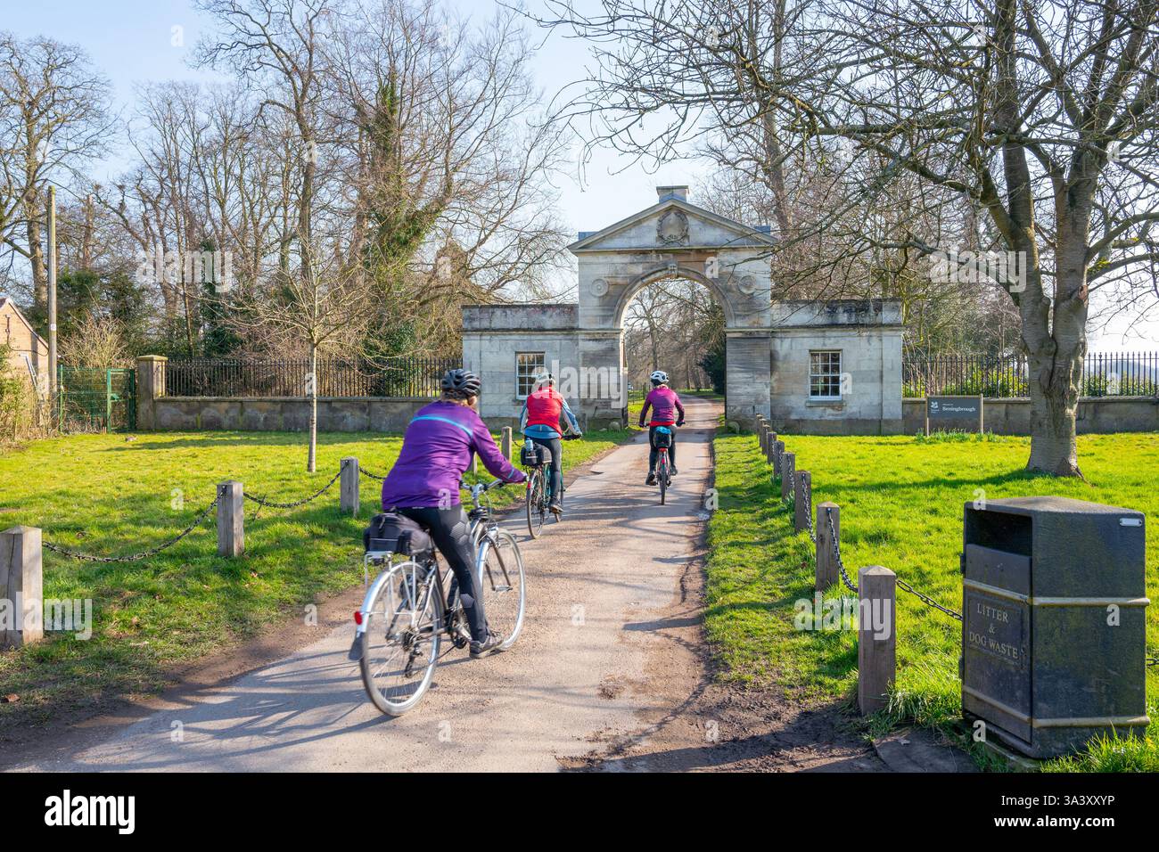 Tre ciclisti donne che entrano nel parco attraverso una porta di ingresso ad arco costruita in pietra a Beningbrough Hall, Newton su Ouse, North Yorkshire. Foto Stock