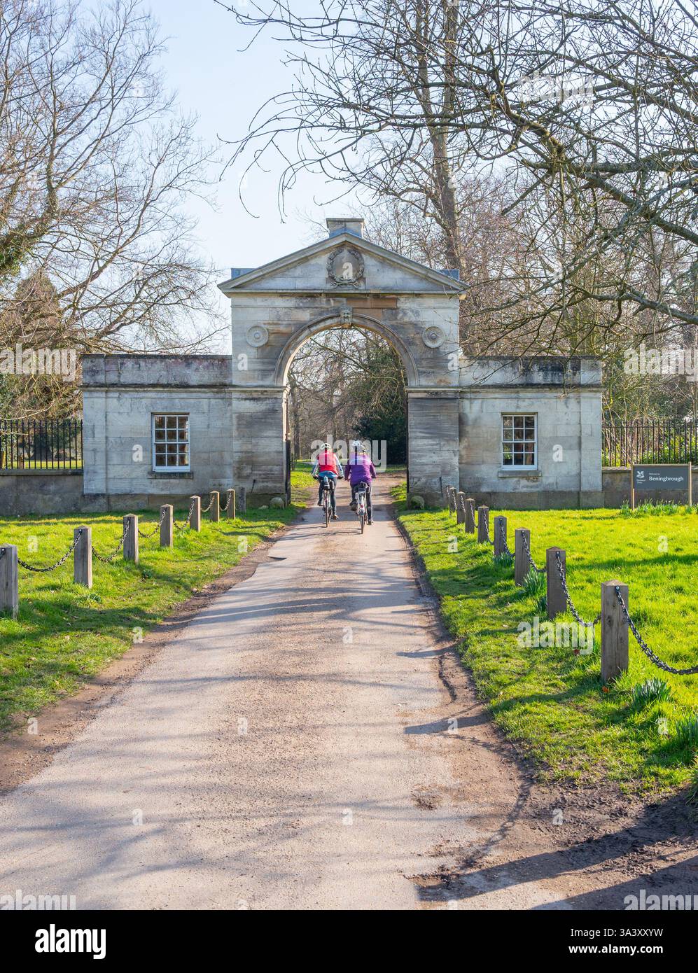 Tre ciclisti donne che entrano nel parco attraverso una porta di ingresso ad arco costruita in pietra a Beningbrough Hall, Newton su Ouse, North Yorkshire. Foto Stock