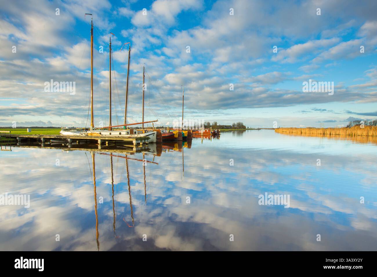 Splendidi riflessi delle nuvole in un canale con barche a vela nel porto in una giornata tranquilla e tranquilla con luce solare brillante e colori vivaci. Foto Stock Splendidi riflessi delle nuvole in un canale con barche a vela nel porto in una giornata tranquilla e tranquilla con luce solare brillante e colori vivaci. Foto Stock