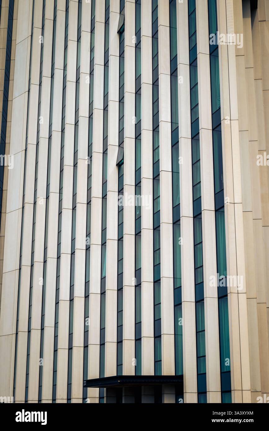 Un primo piano di un alto edificio moderno cattura la sua impressionante facciata in cemento e vetro, linee verticali audaci formano un ritmico, un motivo di luce e ombra Foto Stock
