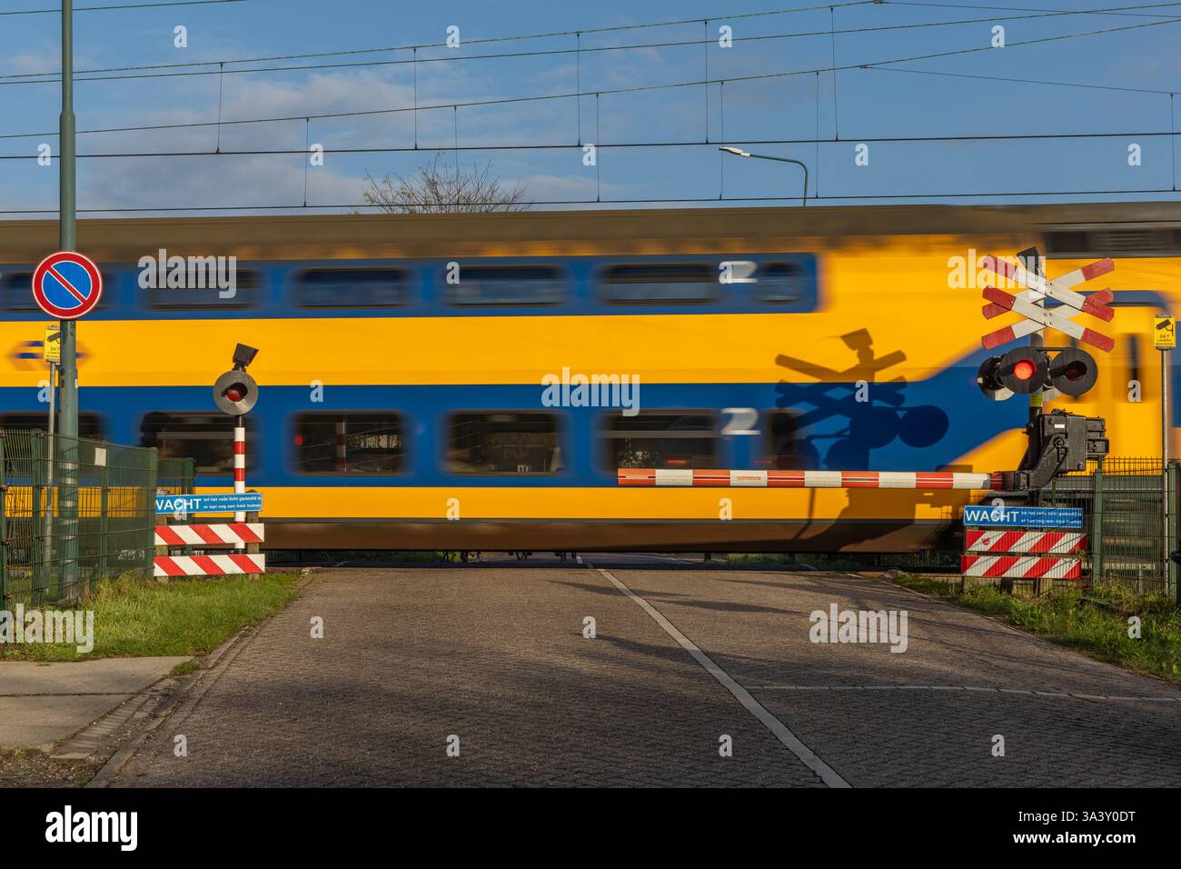 Attraversamento ferroviario su una strada rurale, segnale di stop e semafori, attraversamento di barriere e passaggio di un treno, fattorie e campagna olandese sullo sfondo. Foto Stock