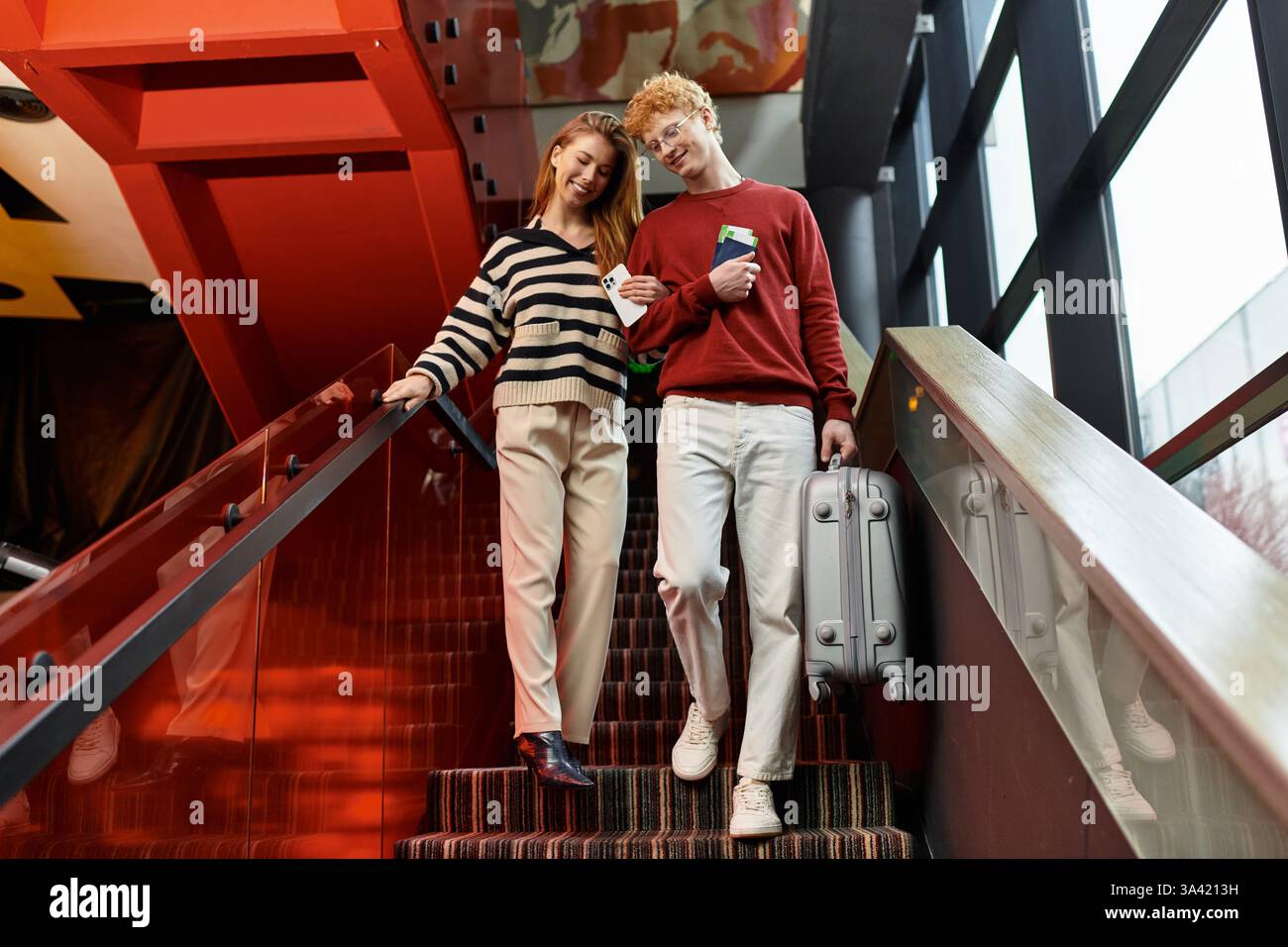 La coppia è felice di scendere le scale dell'hotel, condividere i sorrisi e tenere insieme l'essenziale per il viaggio. Foto Stock