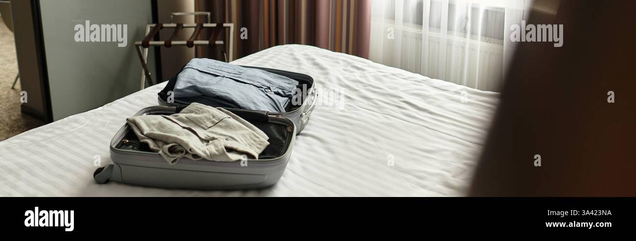 Camera comoda e ben illuminata con un letto e bagagli in valigia. Foto Stock