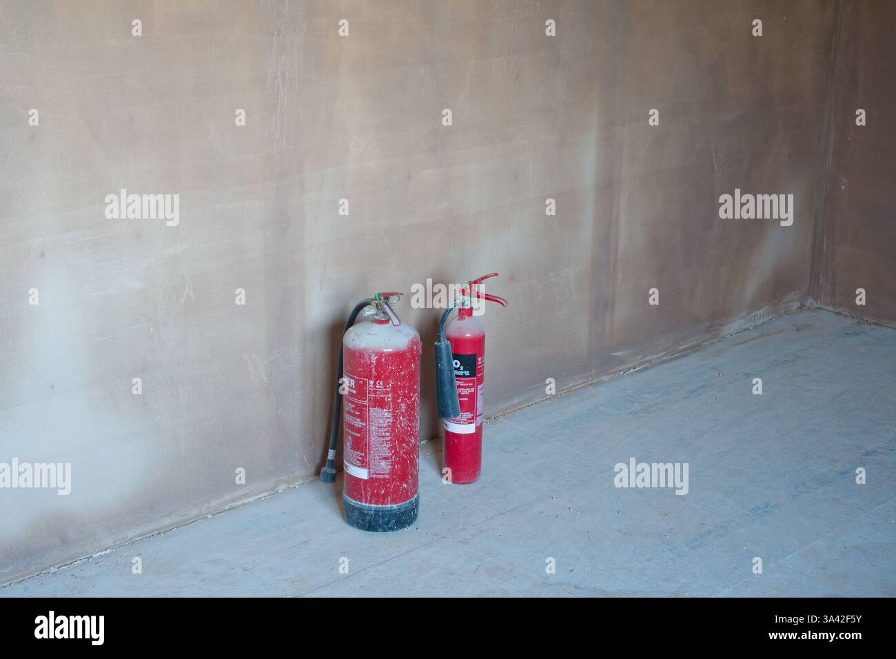Camera intonacata di recente con 2 estintori rossi. Lavori di costruzione rifiniti con una superficie liscia e piatta di intonaco sottile. Una grande abilità. Foto Stock